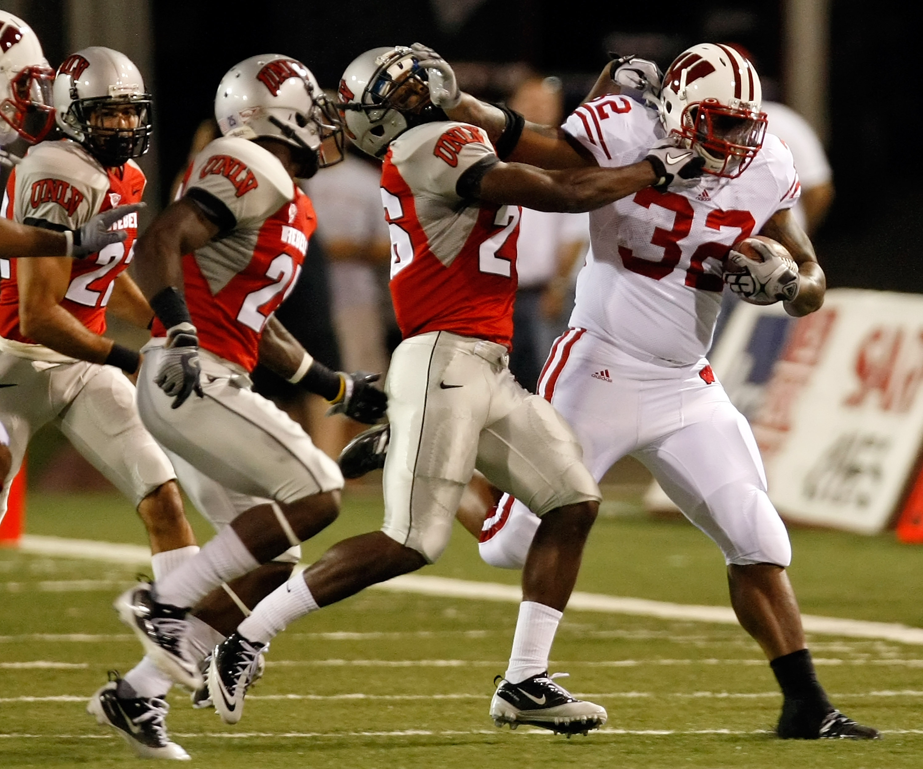 LAS VEGAS - SEPTEMBER 04:  John Clay #32 of the Wisconsin Badgers tries to get away from Deante' Purvis #26 of the UNLV Rebels during the first quarter of their game at Sam Boyd Stadium September 4, 2010 in Las Vegas, Nevada.  (Photo by Ethan Miller/Getty