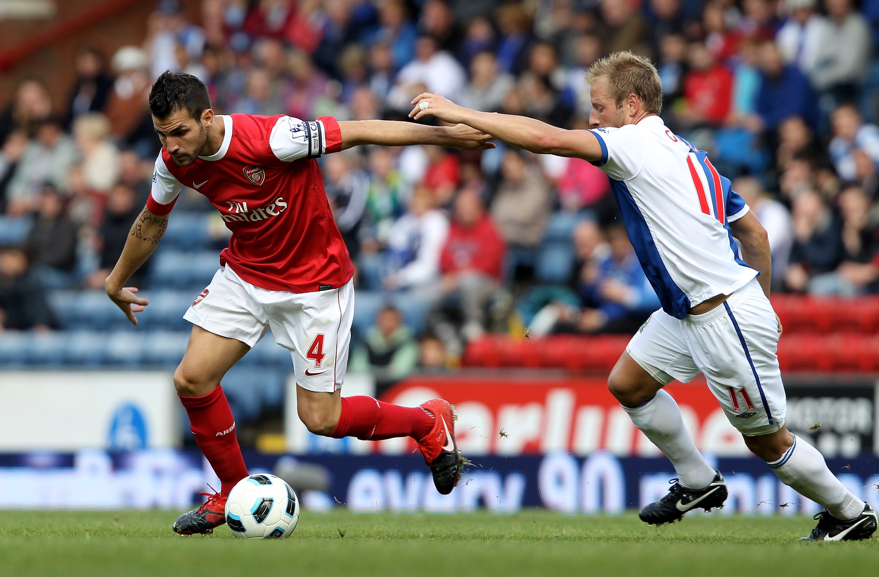 BLACKBURN, ENGLAND - AUGUST 28:   Cesc Fabregas of Arsenal holds off the challenge of Vince Grella of Blackburn Rovers during the Barclays Premier League match between Blackburn Rovers and Arsenal at Ewood Park on August 28, 2010 in Blackburn, England. (P