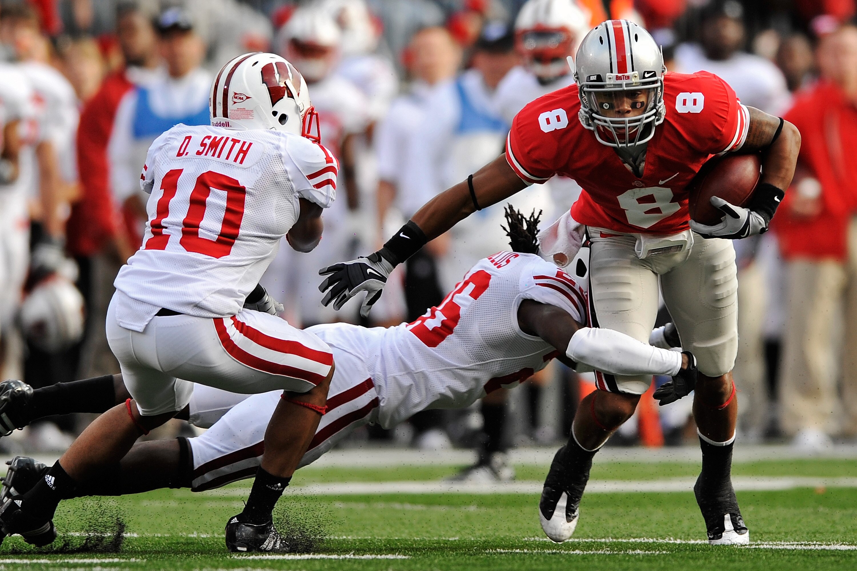 COLUMBUS, OH - OCTOBER 10:  DeVier Posey #8 of the Ohio State Buckeyes attempts to break the tackle of Antonio Fenelus #26 of the Wisconsin Badgers as Devin Smith #10 of the Badgers moves in at Ohio Stadium on October 10, 2009 in Columbus, Ohio.  (Photo b