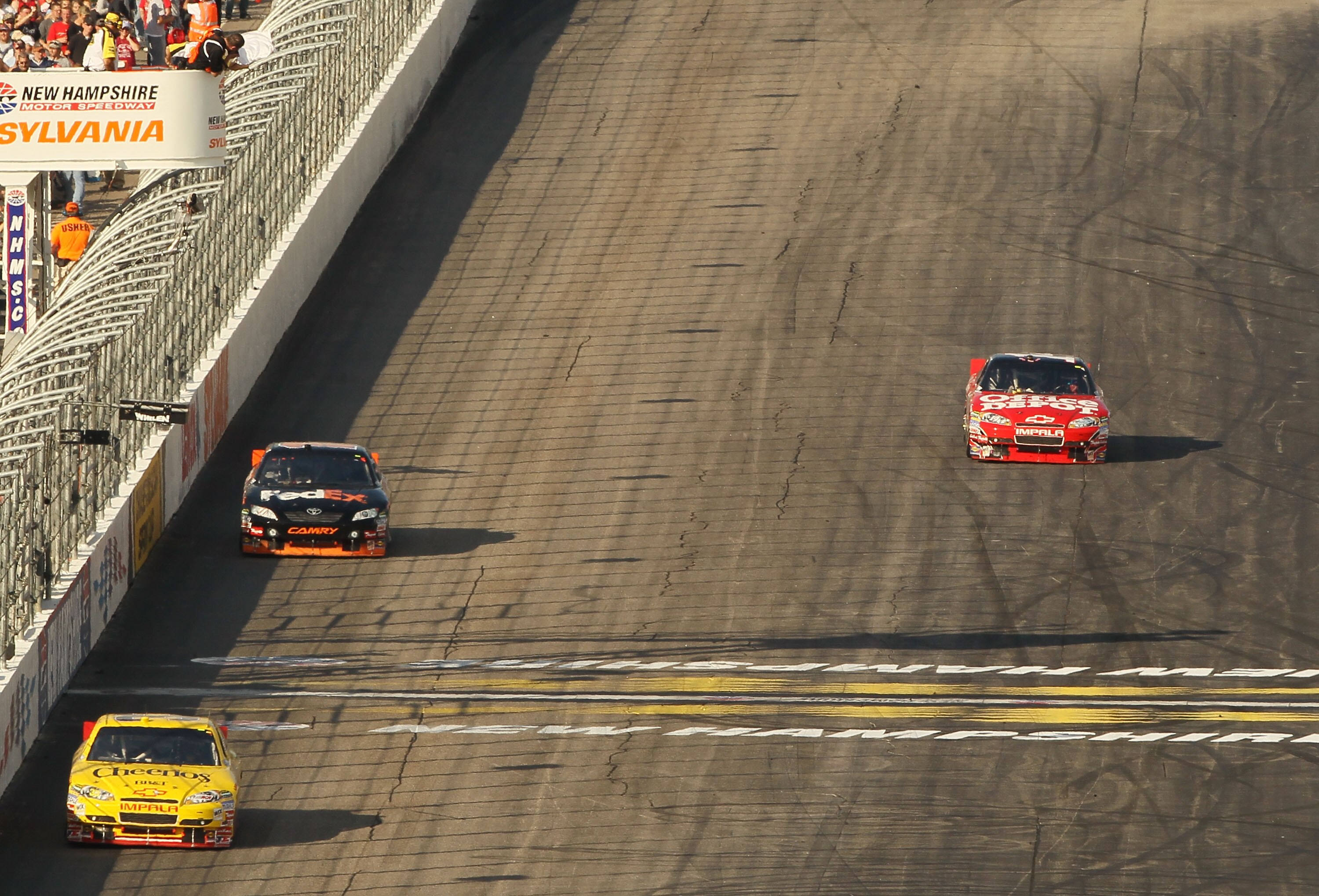 LOUDON, NH - SEPTEMBER 19:  Clint Bowyer, driver of the #33 Cheerios/Hamburger Helper Chevrolet, takes the white flag ahead of Denny Hamlin, driver of the #11 FedEx Small Business Toyota as Tony Stewart, driver of the #14 Office Depot/Old Spice Chevrolet