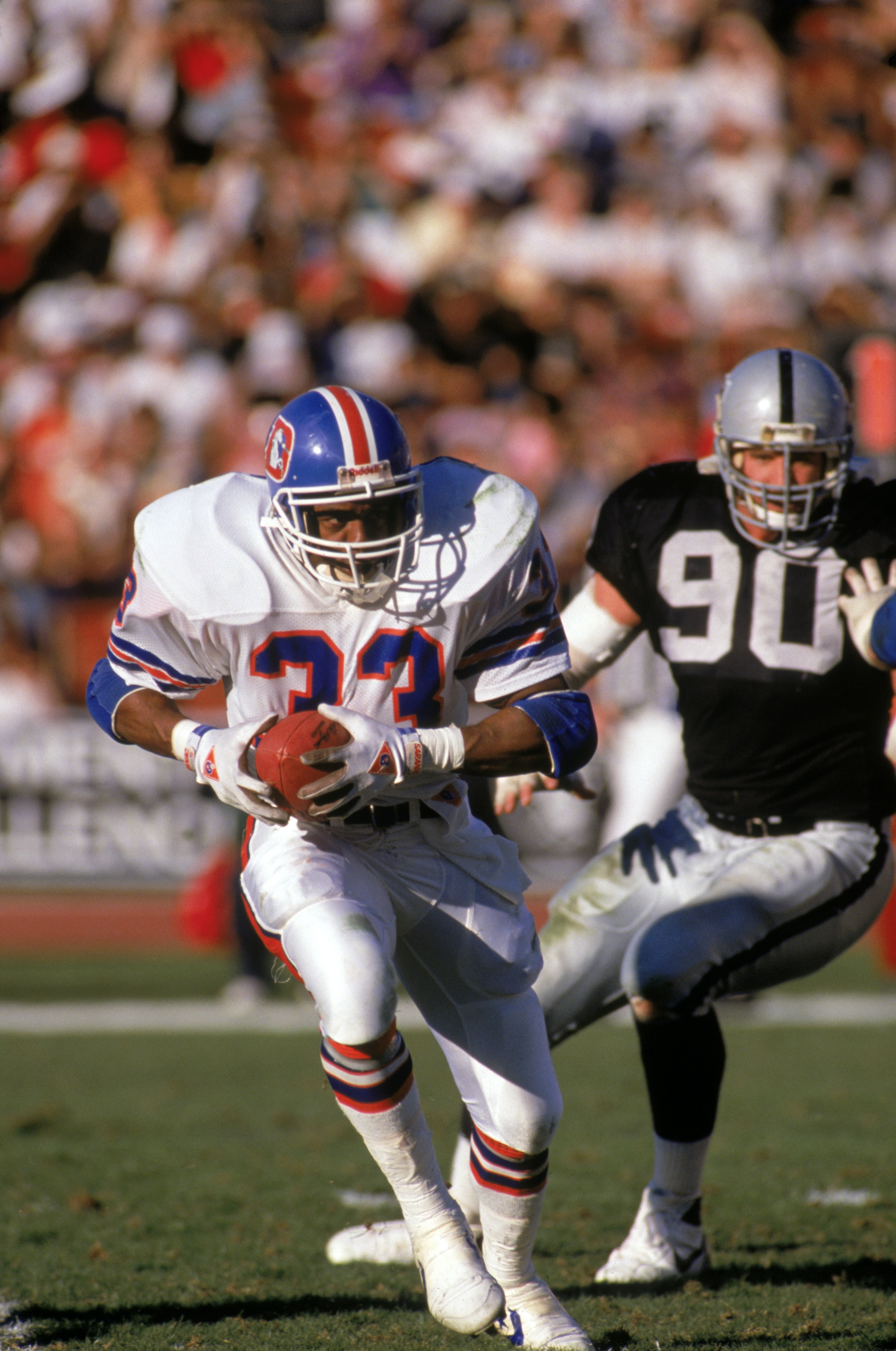 LOS ANGELES - DECEMBER 4:  Running back Tony Dorsett #33 of the Denver Broncos runs away from defensive end Mike Wise #90 of the Los Angeles Raiders during a game at the Los Angeles Memorial Coliseum on December 4, 1988 in Los Angeles, California.  The Ra