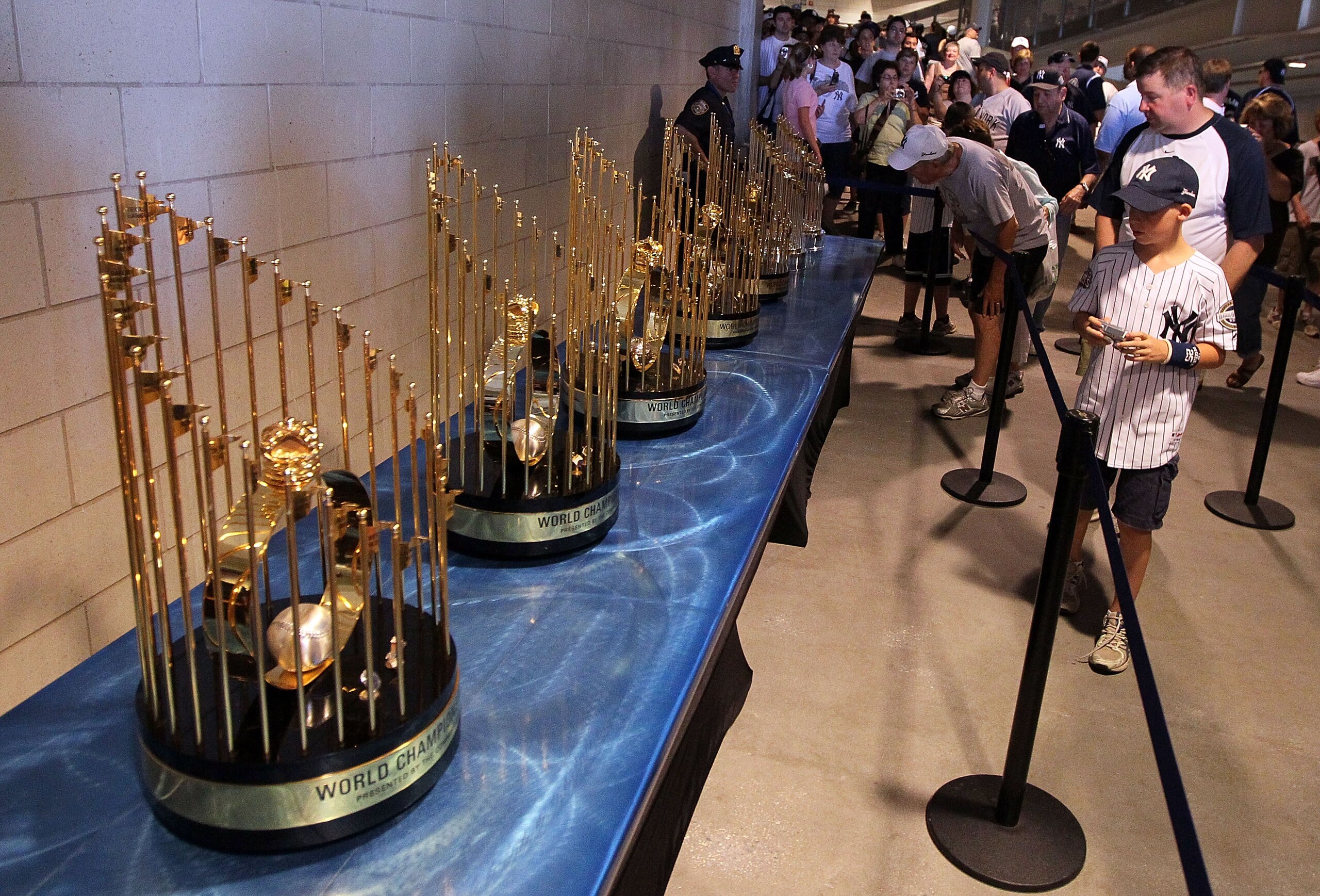 NEW YORK - JULY 04:  Fans photograph the seven World Series championship trophies won by the New York Yankees under the ownership of George Steinbrenner prior to the game against the Toronto Blue Jays on July 4, 2010 at Yankee Stadium in the Bronx borough