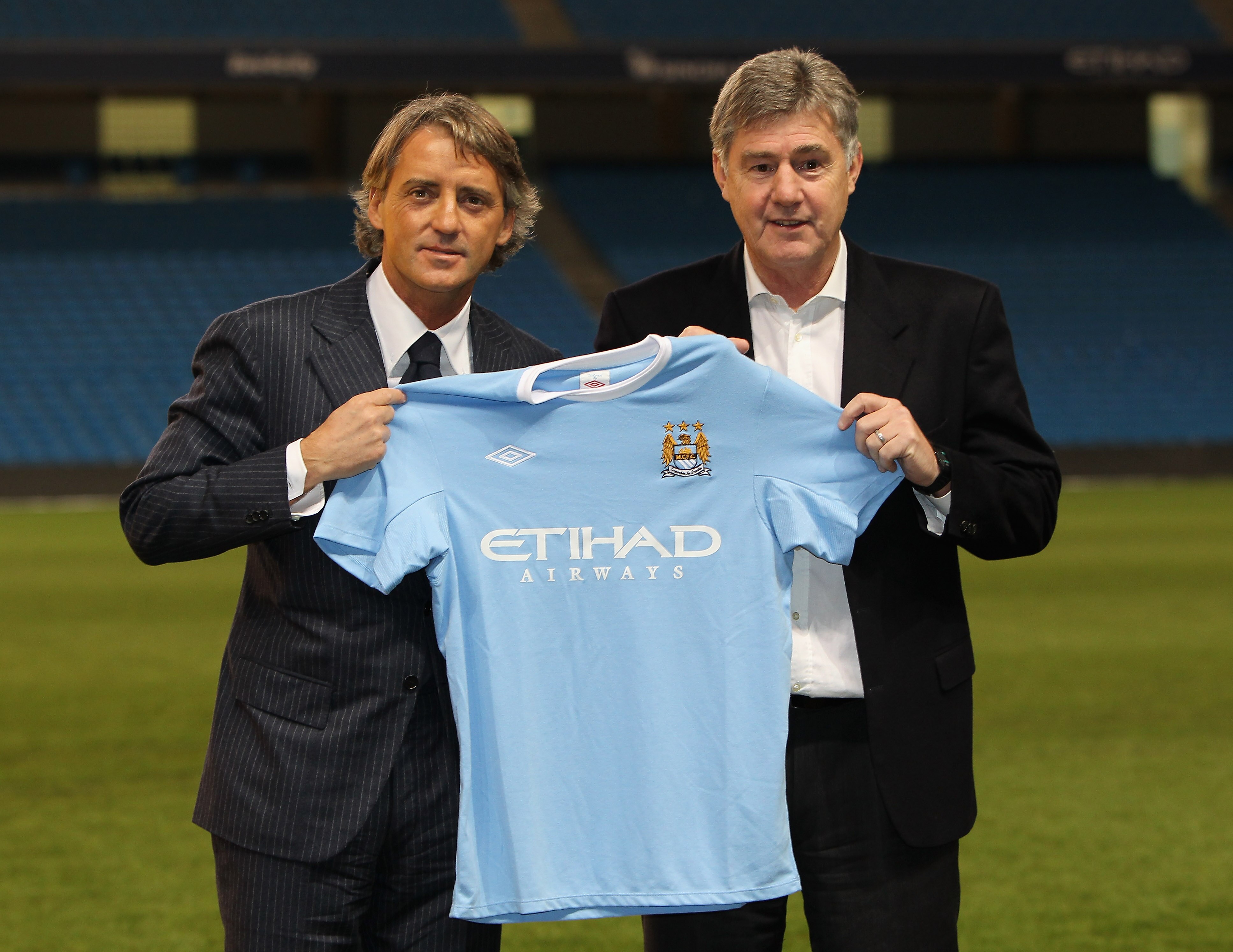 MANCHESTER, ENGLAND - DECEMBER 21:  Roberto Mancini the new manager of Manchester City and his assistant, Brian Kidd, hold up a Manchester City shirt during a photocall after a press conference held at the City of Manchester Stadium on December 21, 2009 i
