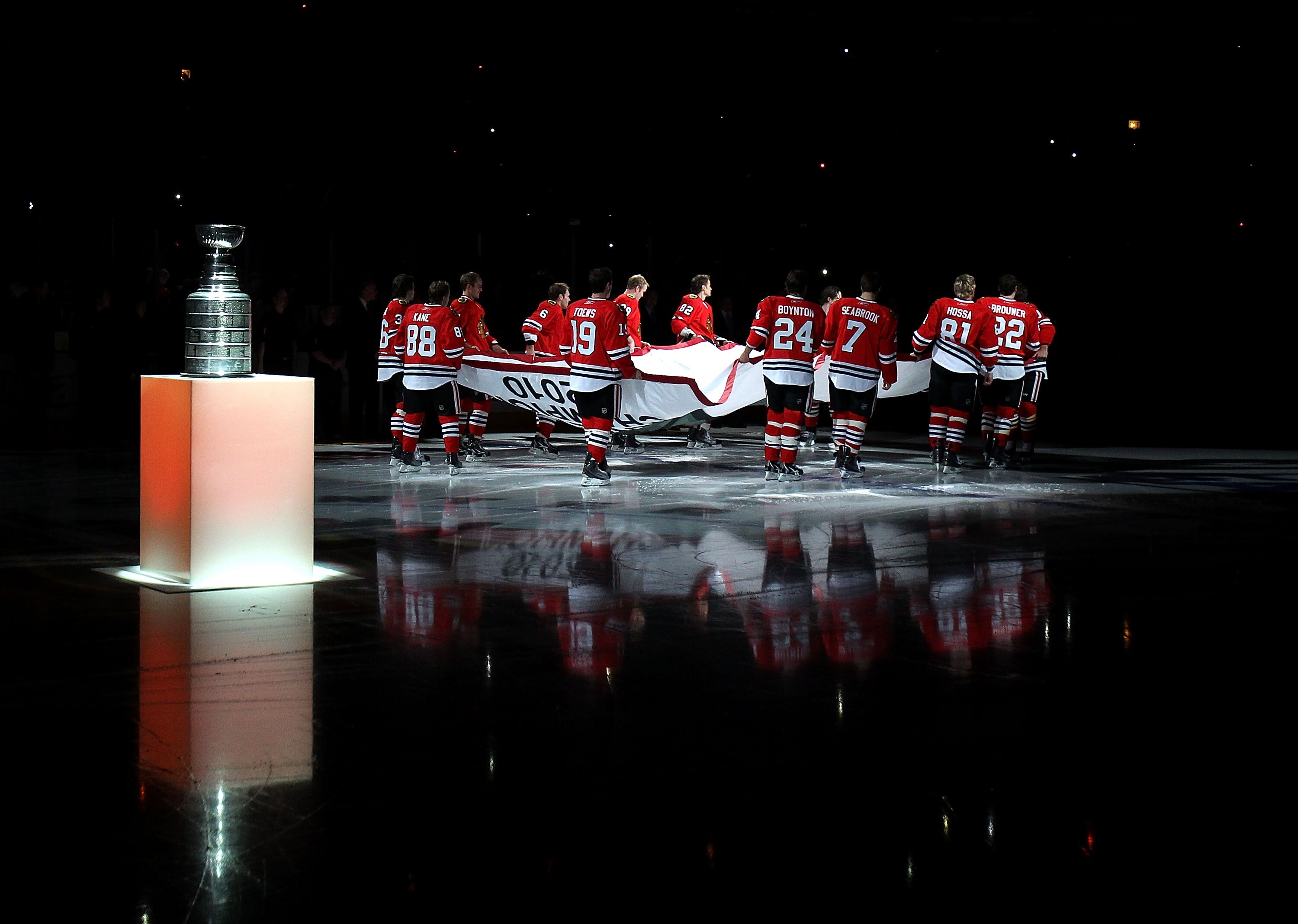CHICAGO - OCTOBER 09: Members of the Chicago Blackhawks carry the Stanley Cup Championship banner across the ice past the Stanley Cup in a ceremony before the Blackhawks season home opening game against the Detroit Red Wings at the United Center on Octobe