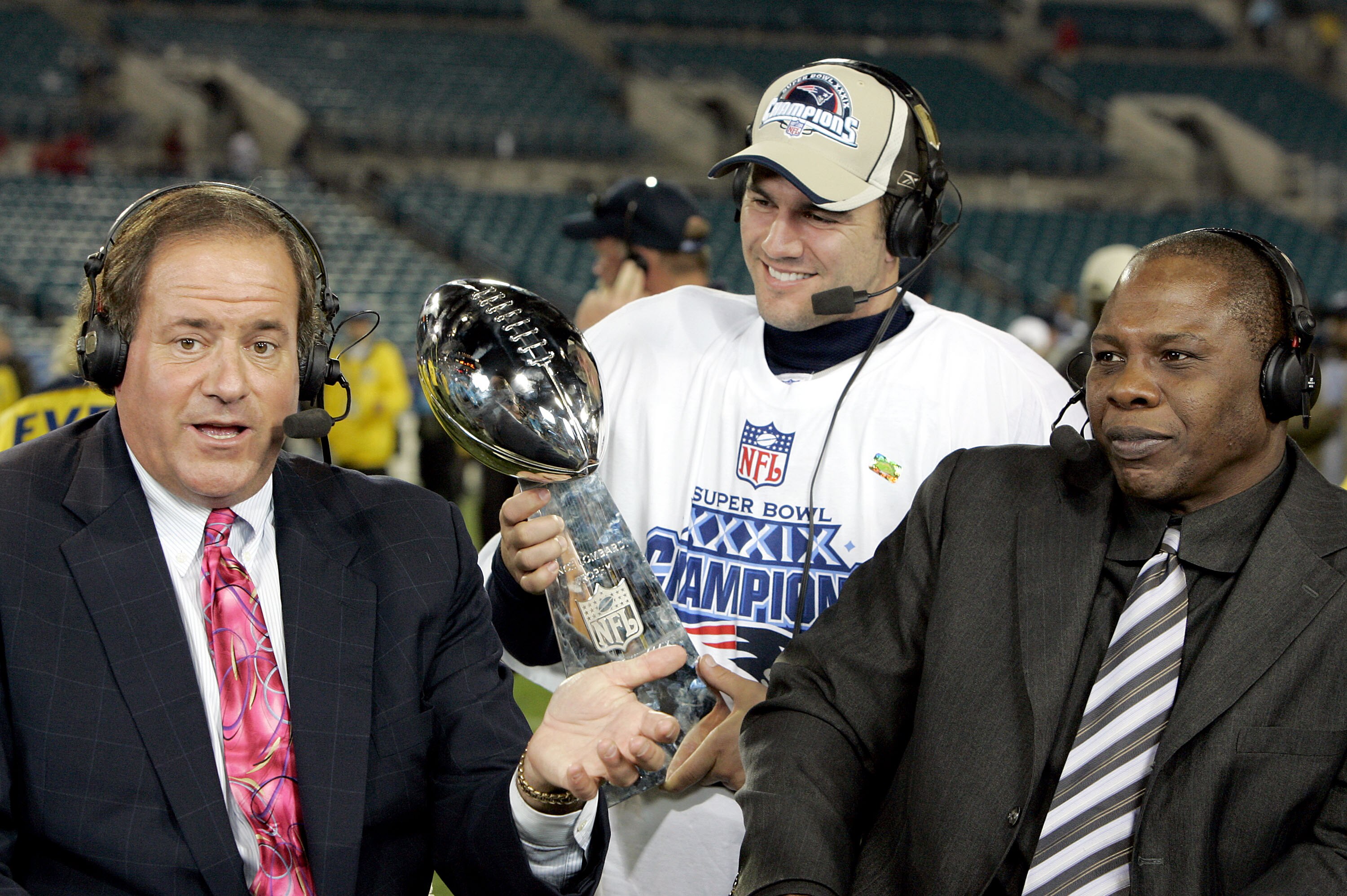 JACKSONVILLE, FL - FEBRUARY 6:  ESPN commentators Chris Berman and Tom Jackson speak while Adam Vinatieri #4 of the New England Patriots celebrates with the Lombardi Trophy after the Patriots defeated the Philadelphia Eagles in Super Bowl XXXIX at Alltel