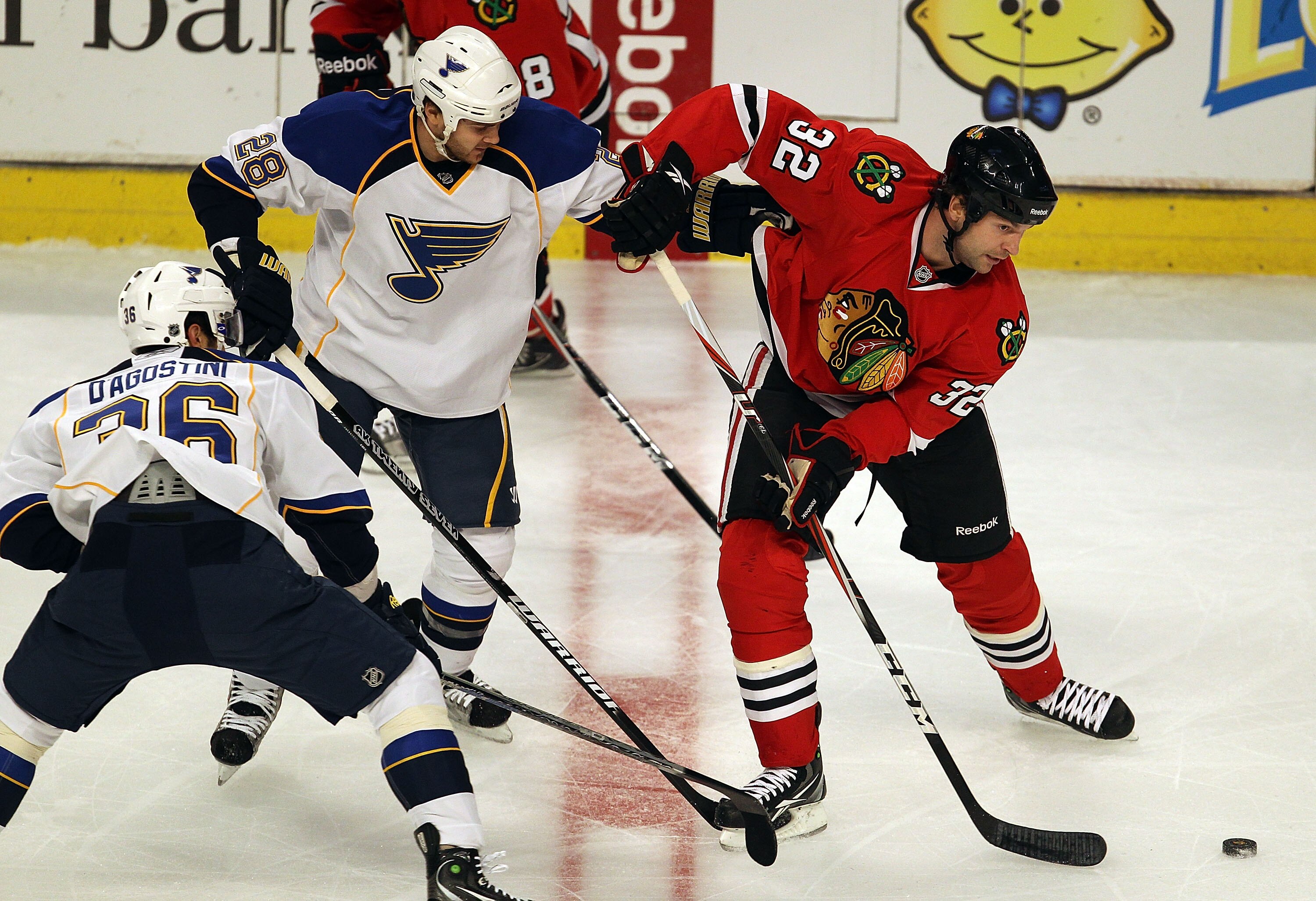 CHICAGO - OCTOBER 18: John Scott #32 of the Chicago Blackhawks looks to pass under pressure from Matt D'Agostini #36 and Carlo Colaiacovo #28 of the St. Louis Blues at the United Center on October 18, 2010 in Chicago, Illinois. The Blackhawks defeated the