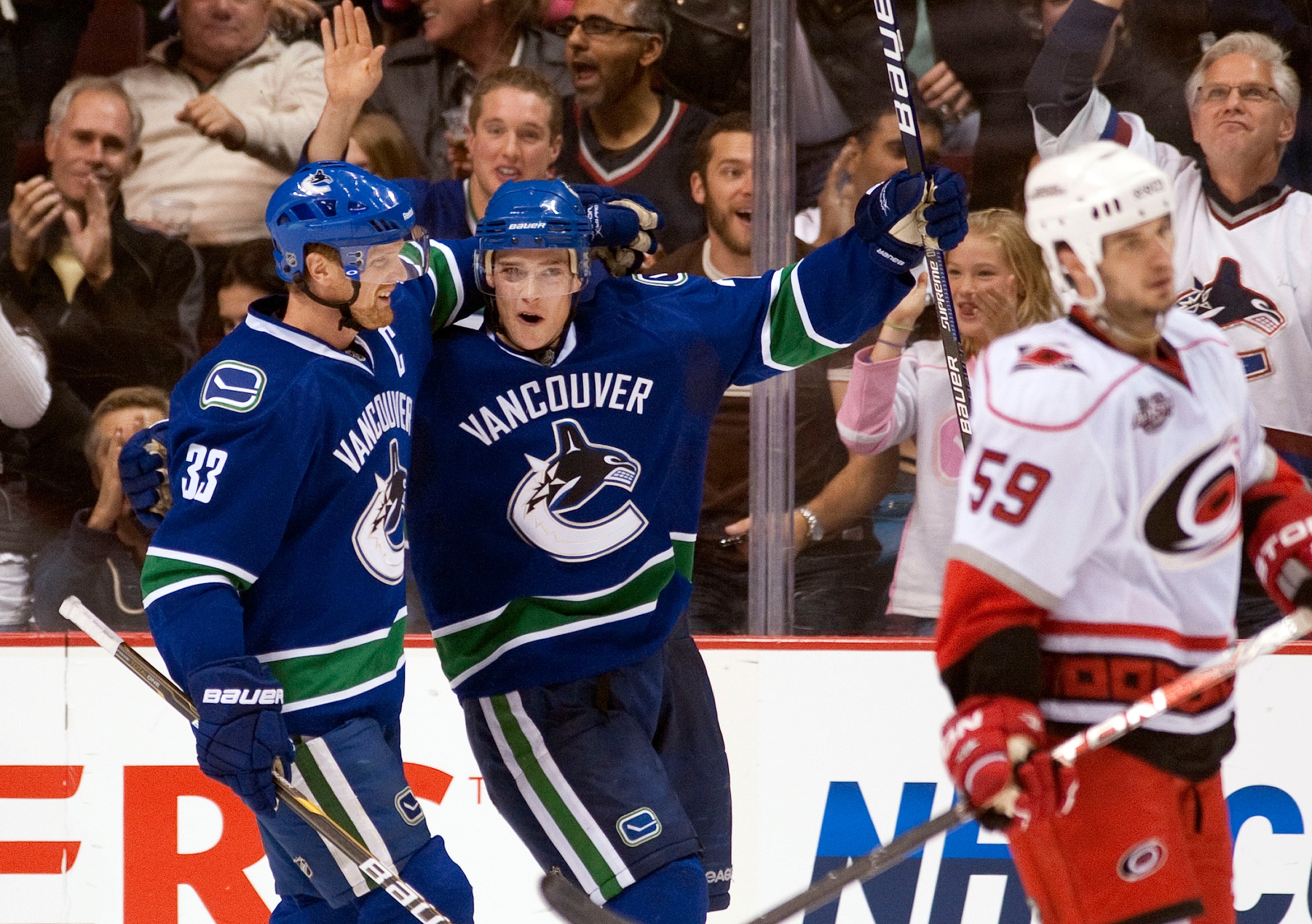 VANCOUVER, CANADA - OCTOBER 17: Mason Rayond #21 of the Vancouver Canucks celebrates with Henrik Sedin #33 while Chad Larose #59 of the Carolina Hurricanes skates by after scoring a goal during the third period in NHL action on October 17, 2010 at Rogers