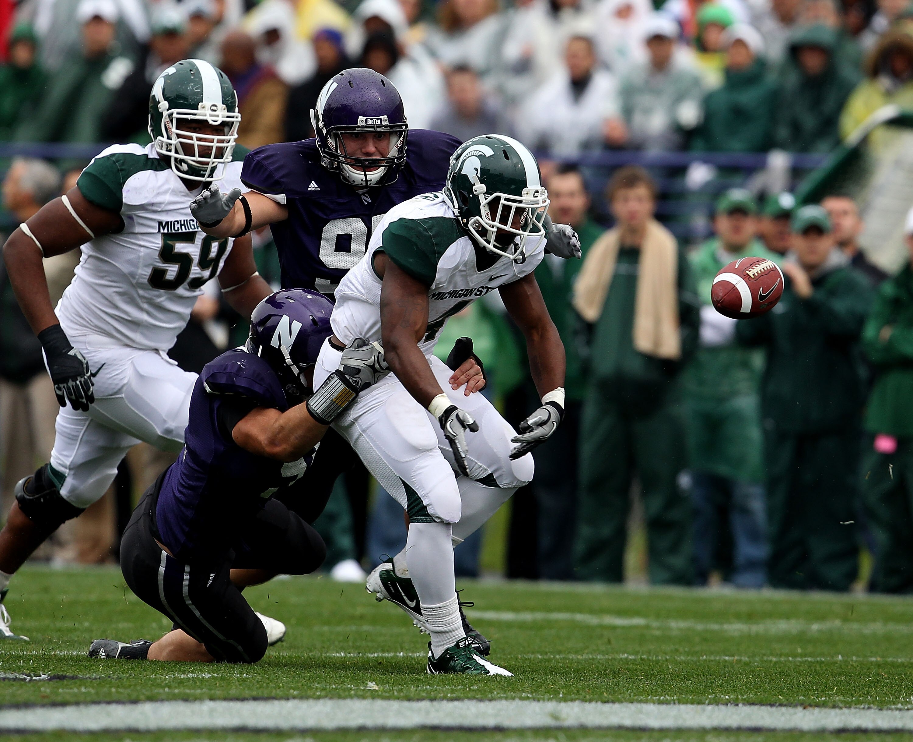 EVANSTON, IL - OCTOBER 23: Edwin Baker #4 of the Michigan State Spartans fumbles the ball as he is hit by Bryce McNaul #51 and Tyler Scott #97 of the Northwestern Wildcats at Ryan Field on October 23, 2010 in Evanston, Illinois. Michigan State defeated No