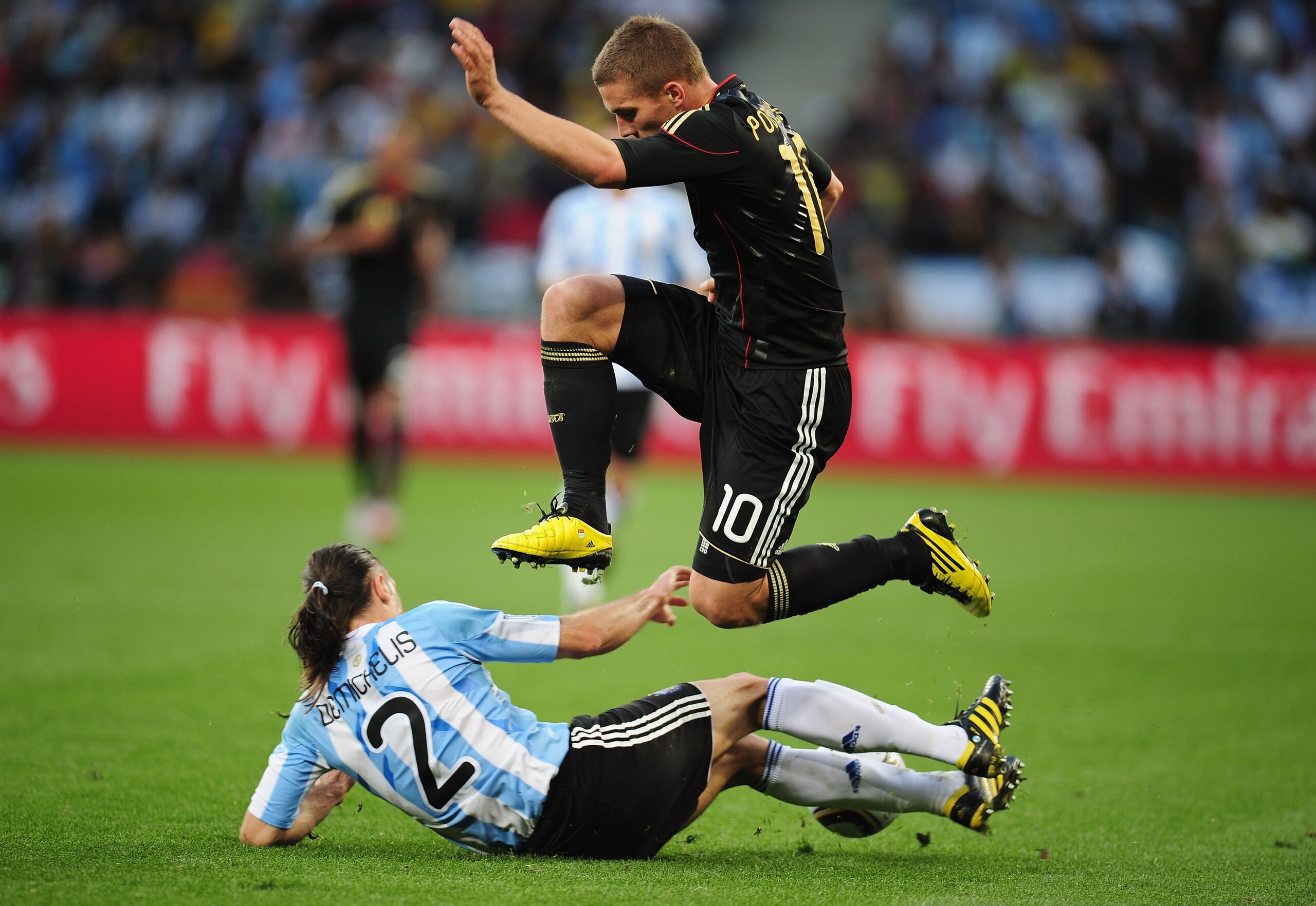 CAPE TOWN, SOUTH AFRICA - JULY 03:  Lukas Podolski of Germany jumps over the challenge of Martin Demichelis of Argentina during the 2010 FIFA World Cup South Africa Quarter Final match between Argentina and Germany at Green Point Stadium on July 3, 2010 i