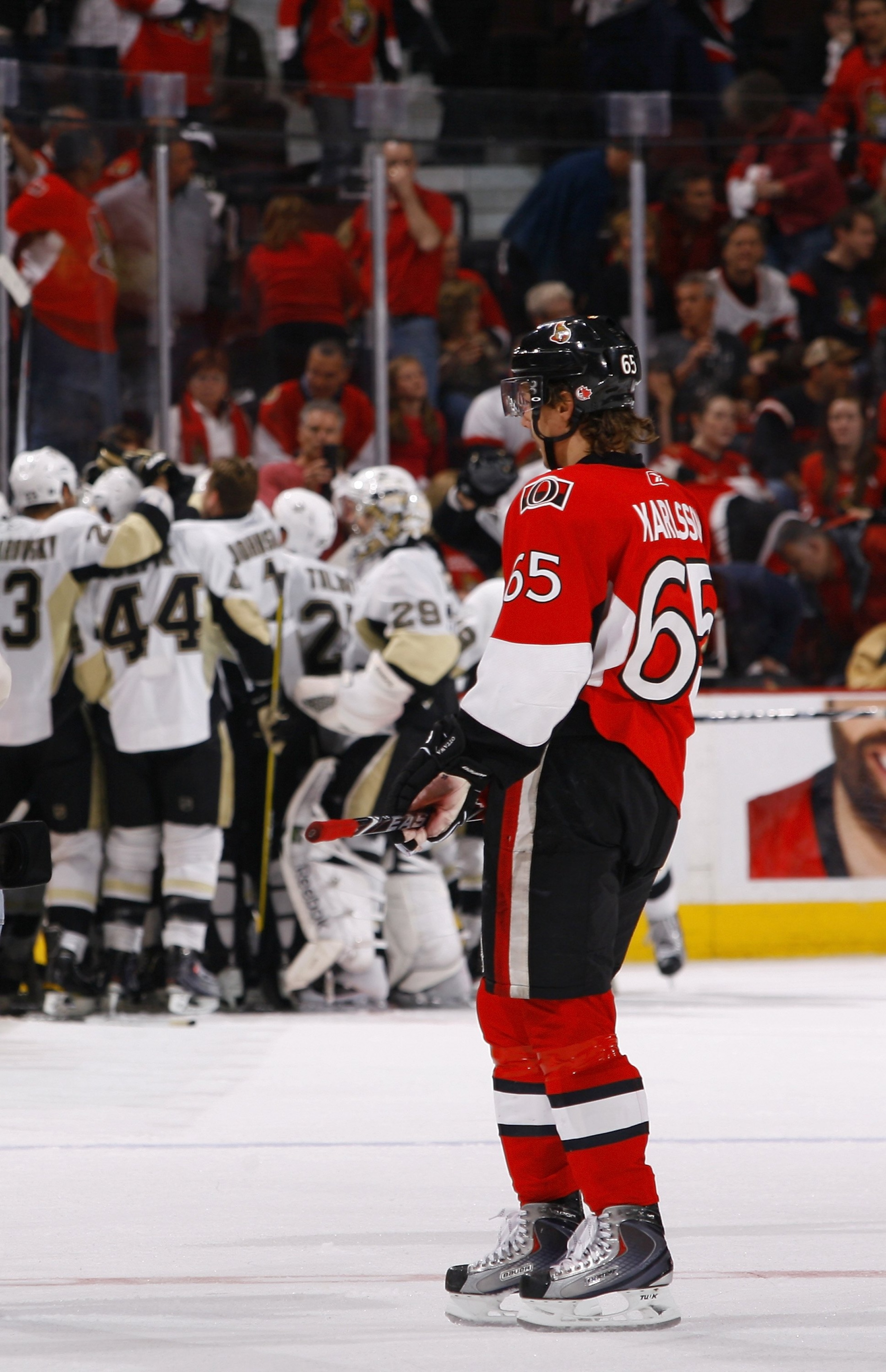 OTTAWA, ON - APRIL 24:  A dejected Erik Karlsson #65 of the Ottawa Senators stands on the ice as the Pittsburgh Penguins celebrate in Game 6 of the Eastern Conference Quaterfinals during the 2010 Stanley Cup Playoffs at Scotiabank Place on April 24, 2010 