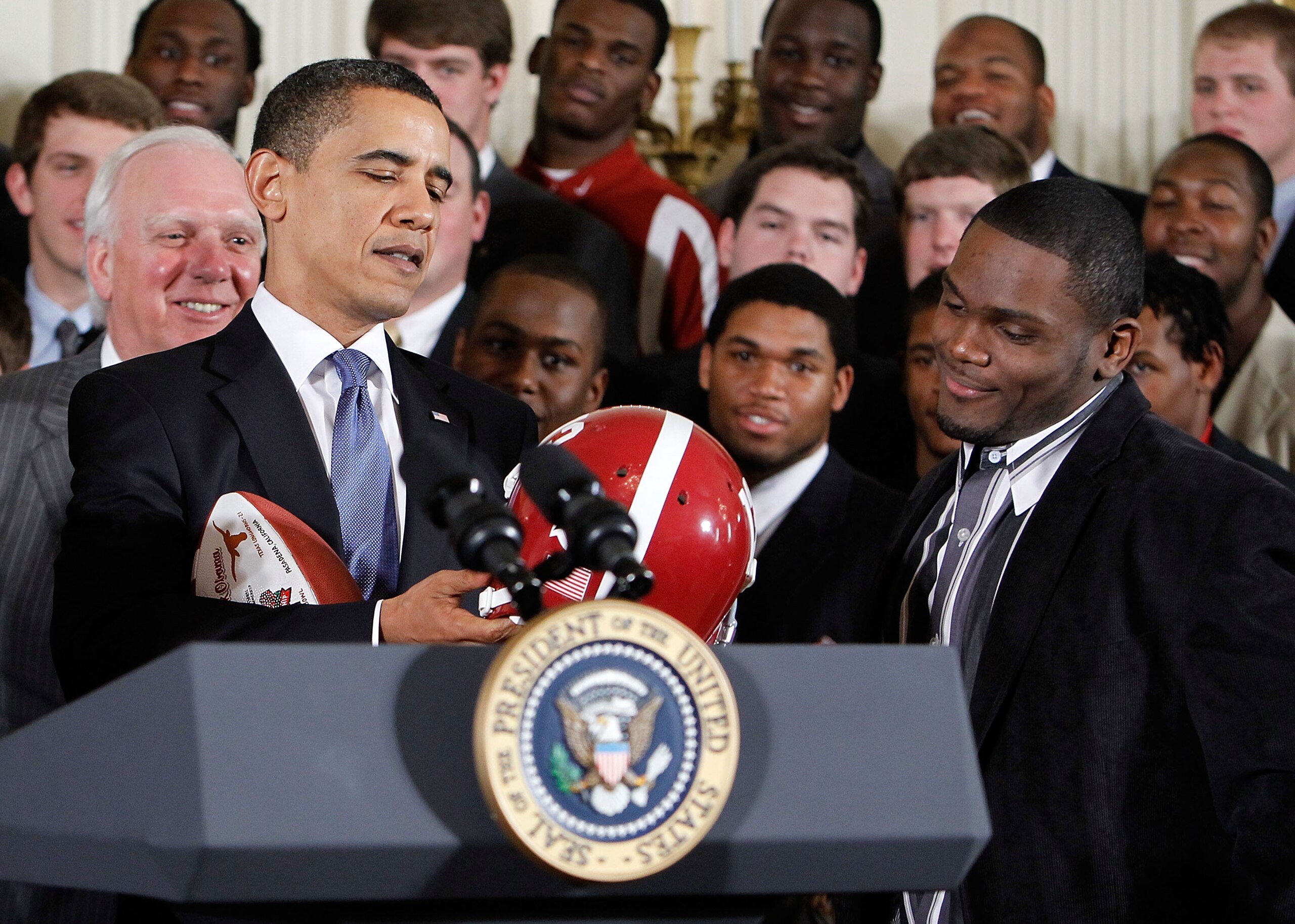 WASHINGTON - MARCH 08:  U.S. President Barack Obama (L) receives a football helmet during an East Room event to host members of the Alabama Crimson Tide March 8, 2010 at the White House in Washington, DC. Obama welcomed the 2009 BCS Champion to honor its