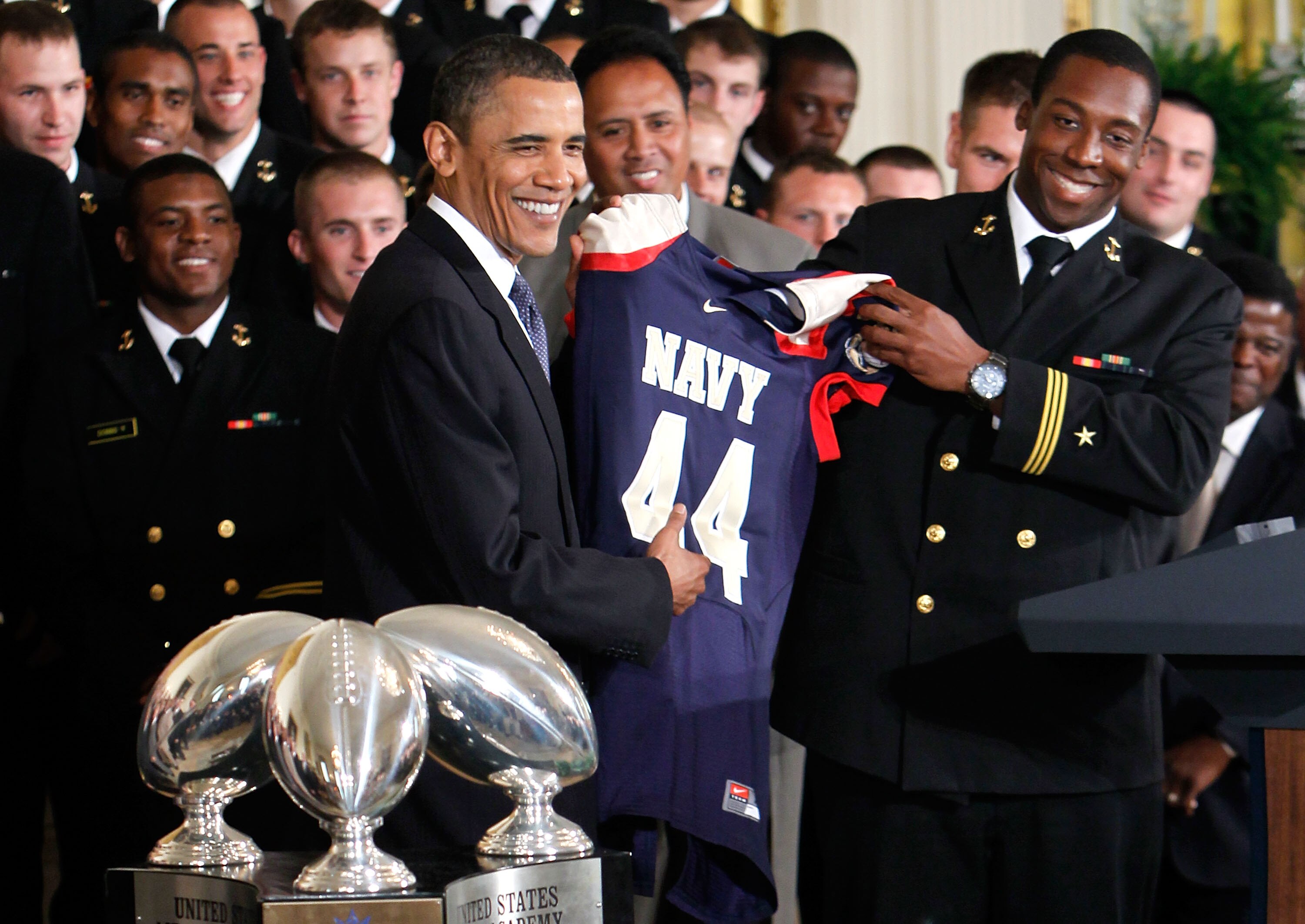 WASHINGTON - MAY 03:  U.S. President Barack Obama (L) receives a jersey from Osei Asante (R) of the Navy football team Midshipmen during the presentation ceremony of the Commander-in-Chief's Trophy at the East Room of the White House May 3, 2010 in Washin