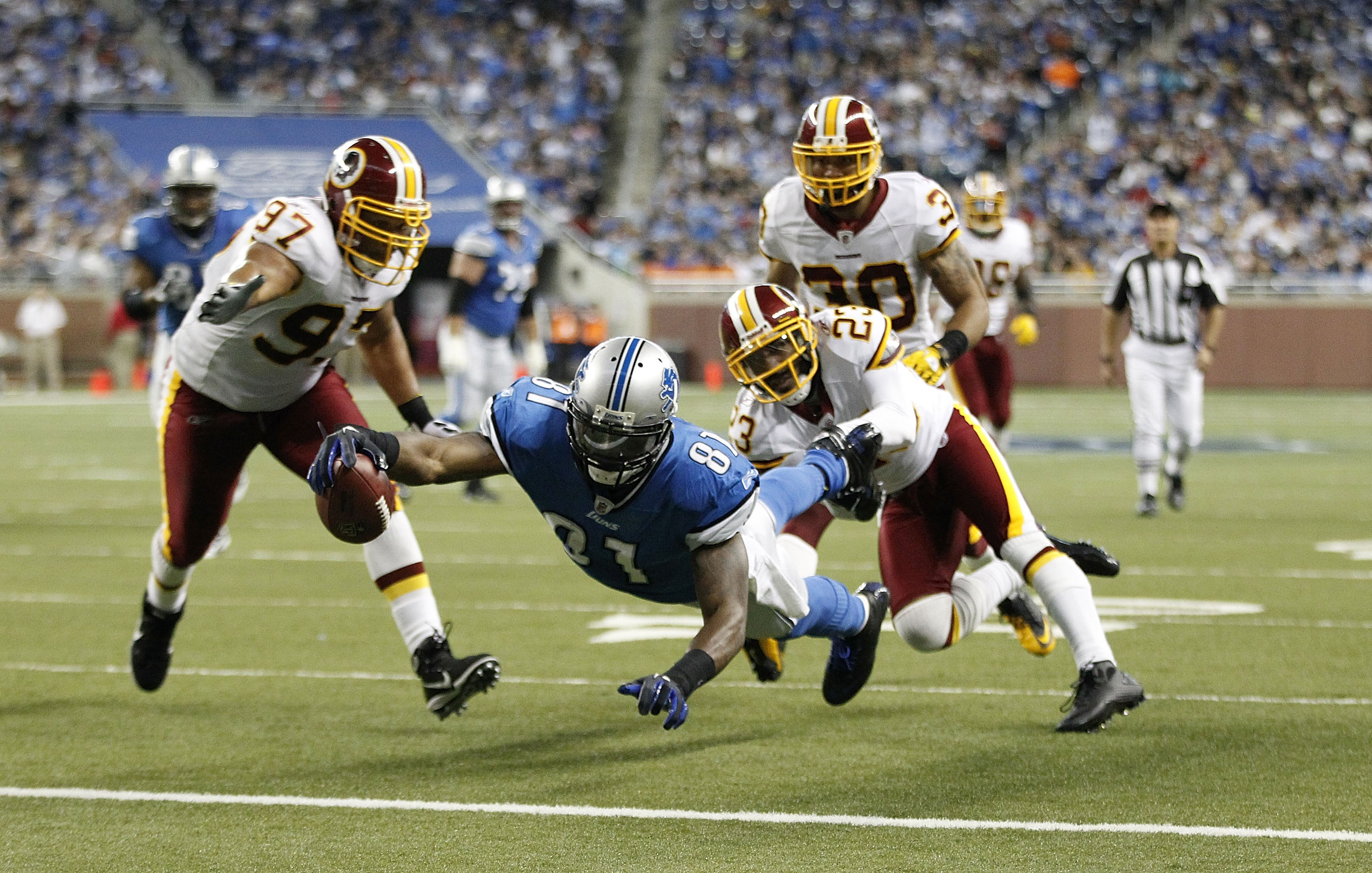 DETROIT - OCTOBER 31: Calvin Johnson #81 of the Detroit Lions scores a second quarter touchdown as DeAngelo Hall #23 and Lorenzo Alexander #97 of the Washington Redskins attempt tp make the stop at Ford Field on October 31, 2010 in Detroit, Michigan. (Pho
