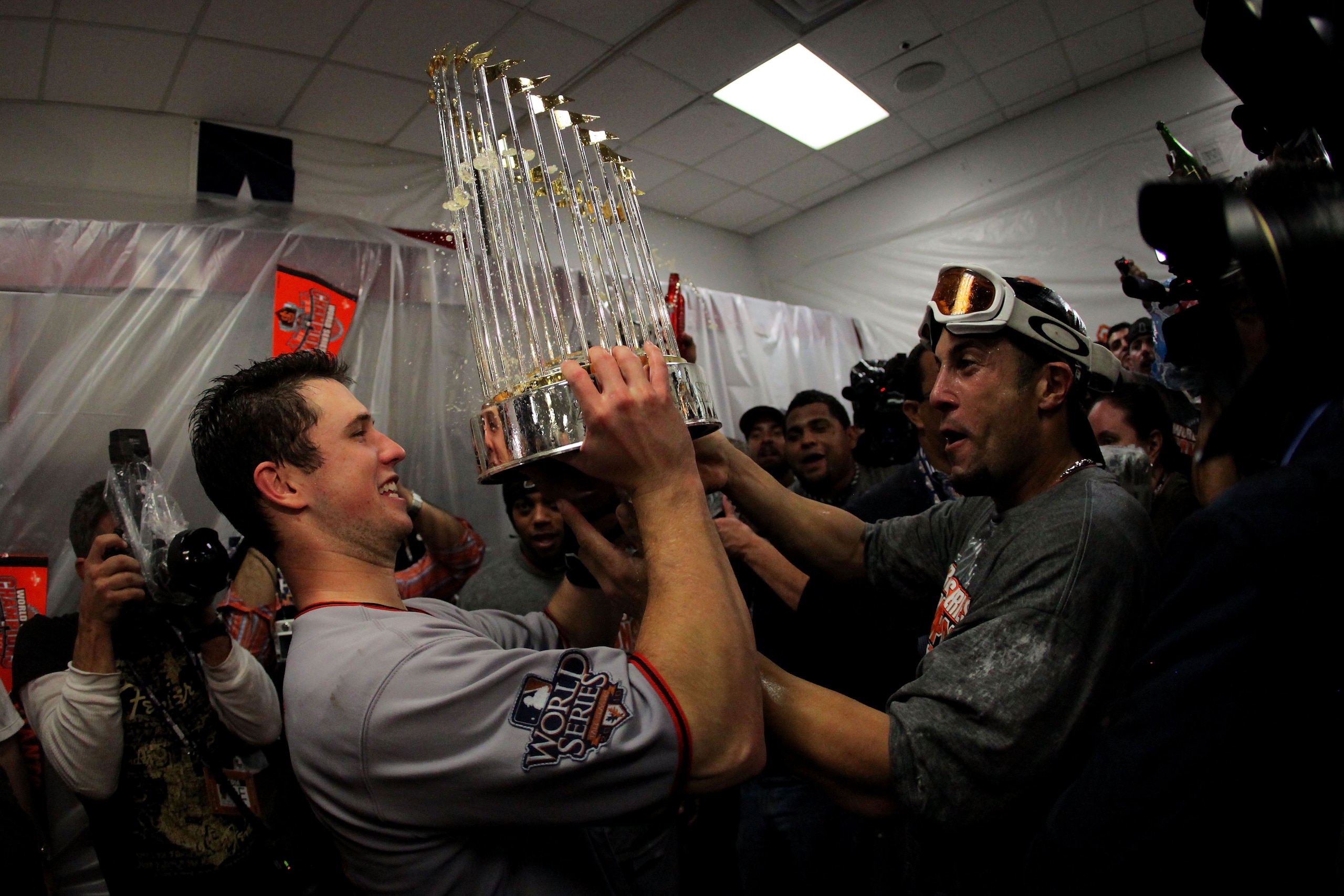 ARLINGTON, TX - NOVEMBER 01:  (L-R) Buster Posey #28 and Andres Torres of the San Francisco Giants celebrates with the trophy in the locker room after the Giants won 3-1 against the Texas Rangers in Game Five of the 2010 MLB World Series at Rangers Ballpa