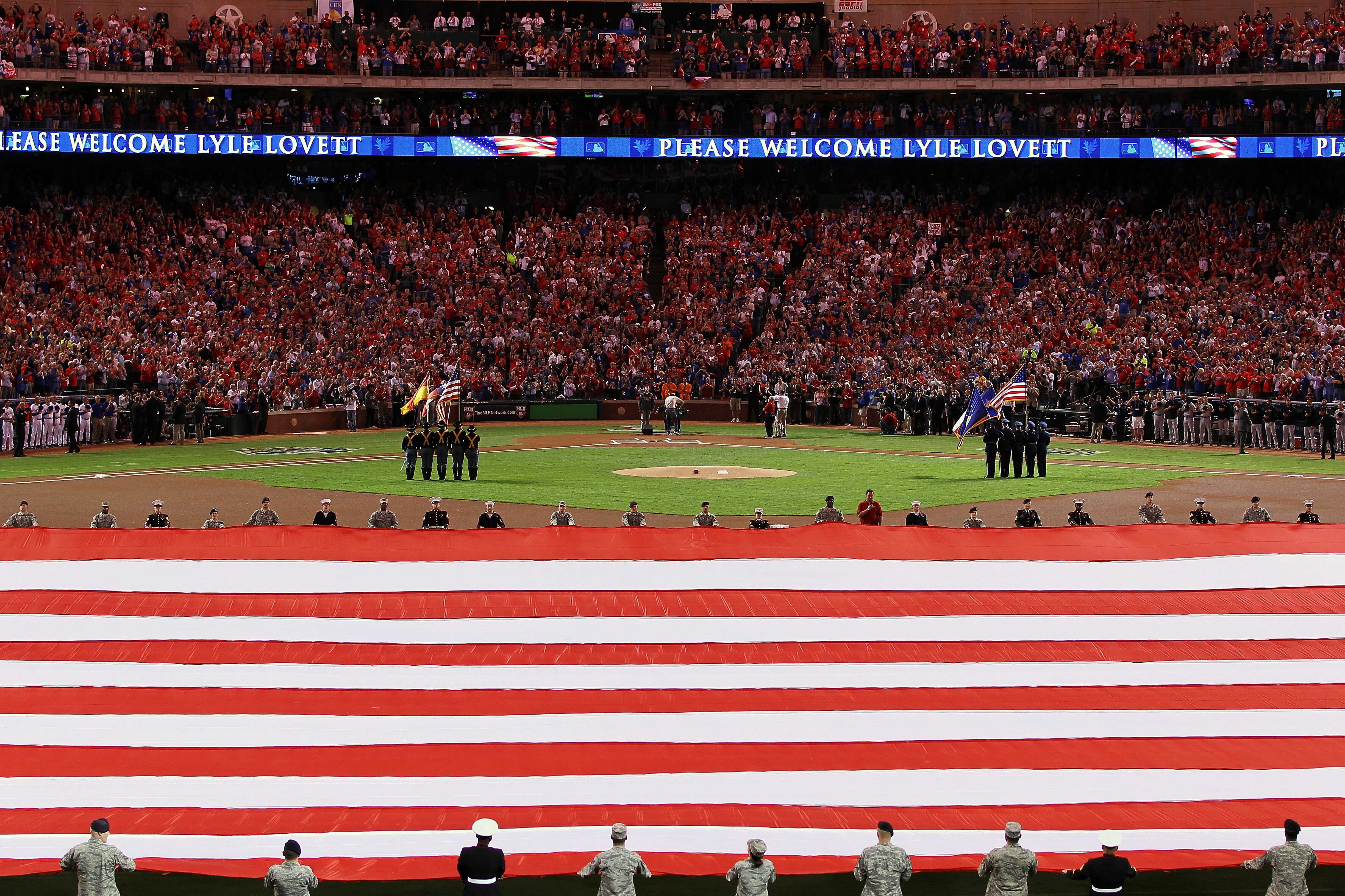 ARLINGTON, TX - OCTOBER 31:  Lyle Lovett performs the National Anthem as a large American Flag is spread across the field prior to the start of Game Four between  the Texas Rangers and the San Francisco Giants during the 2010 MLB World Series at Rangers B