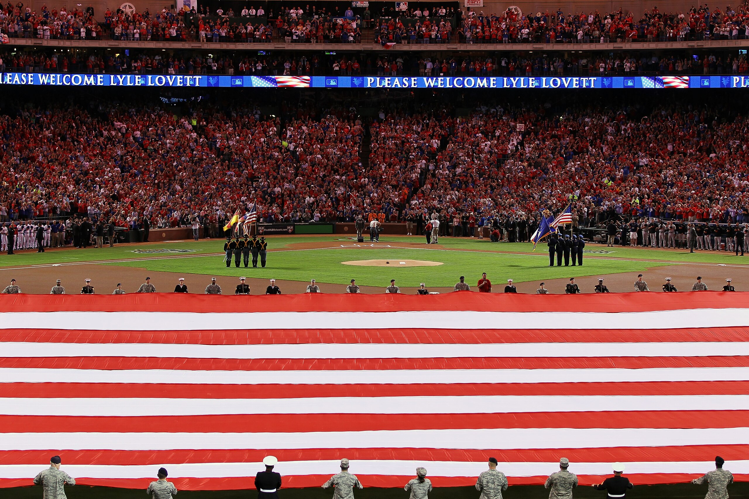 ARLINGTON, TX - OCTOBER 31:  Lyle Lovett performs the National Anthem as a large American Flag is spread across the field prior to the start of Game Four between  the Texas Rangers and the San Francisco Giants during the 2010 MLB World Series at Rangers B