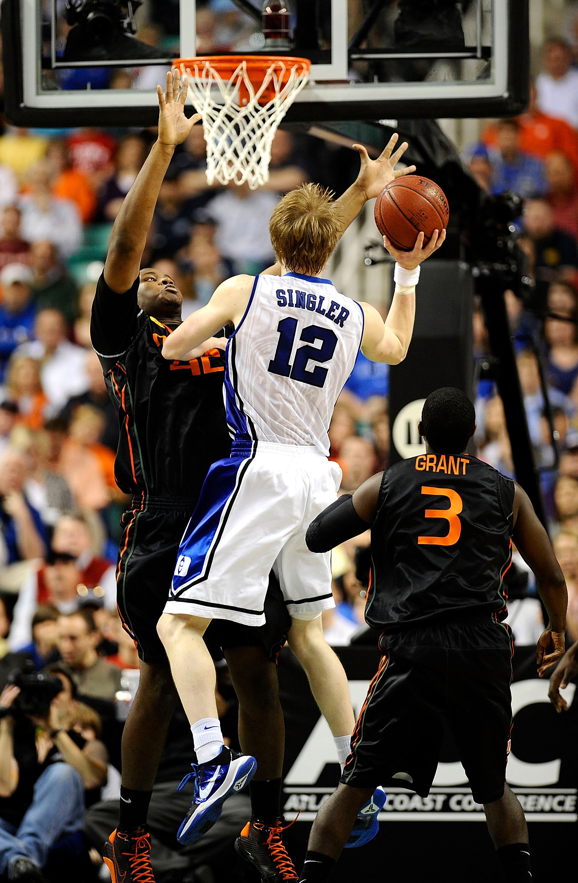 GREENSBORO, NC - MARCH 13:  Kyle Singler #12 of the Duke Blue Devils puts up a shot between Reggie Johnson #32 and Malcolm Grant #3  of the University of Miami Hurricanes in their semifinal game in the 2010 ACC Men's Basketball Tournament at the Greensbor