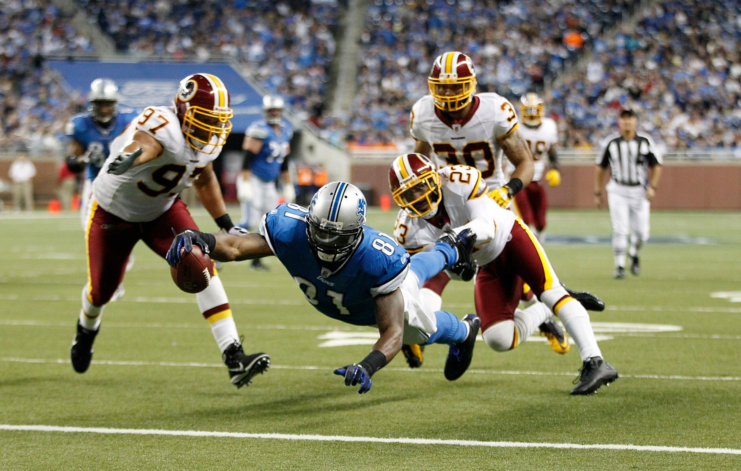 DETROIT - OCTOBER 31: Calvin Johnson #81 of the Detroit Lions scores a second quarter touchdown as DeAngelo Hall #23 and Lorenzo Alexander #97 of the Washington Redskins attempt tp make the stop at Ford Field on October 31, 2010 in Detroit, Michigan. (Pho