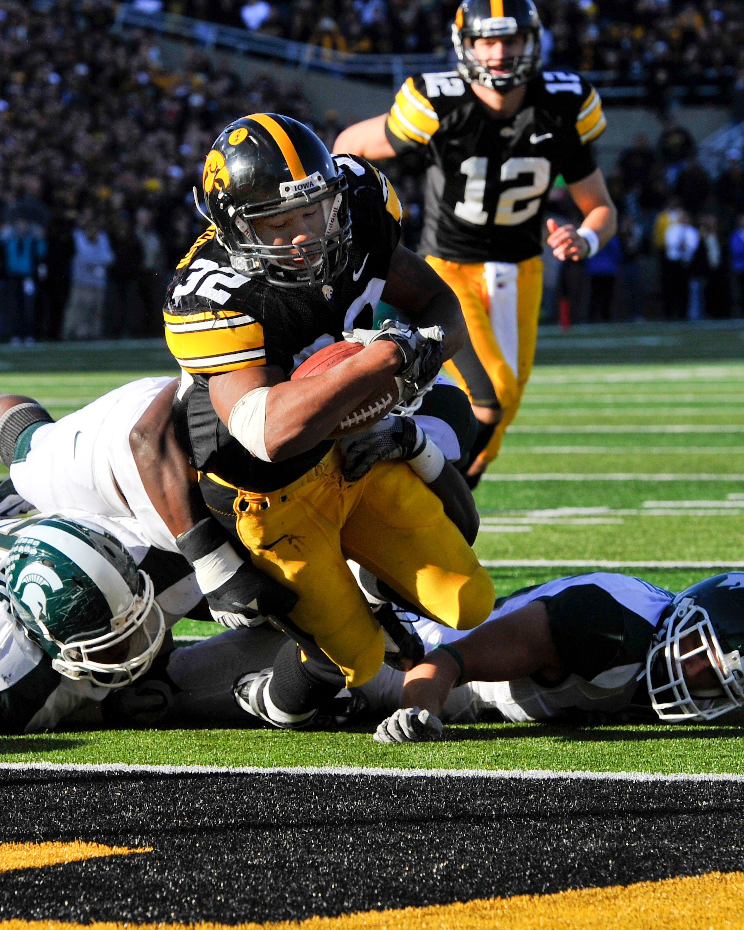 IOWA CITY, IA - OCTOBER 30: Running back Adam Robinson #32 of the University of Iowa Hawkeyes dives into the end zone past Michigan State Spartan defenders for a touch down as quarterback Ricky Stanzi #12 watches on during the first half of play at Kinnic