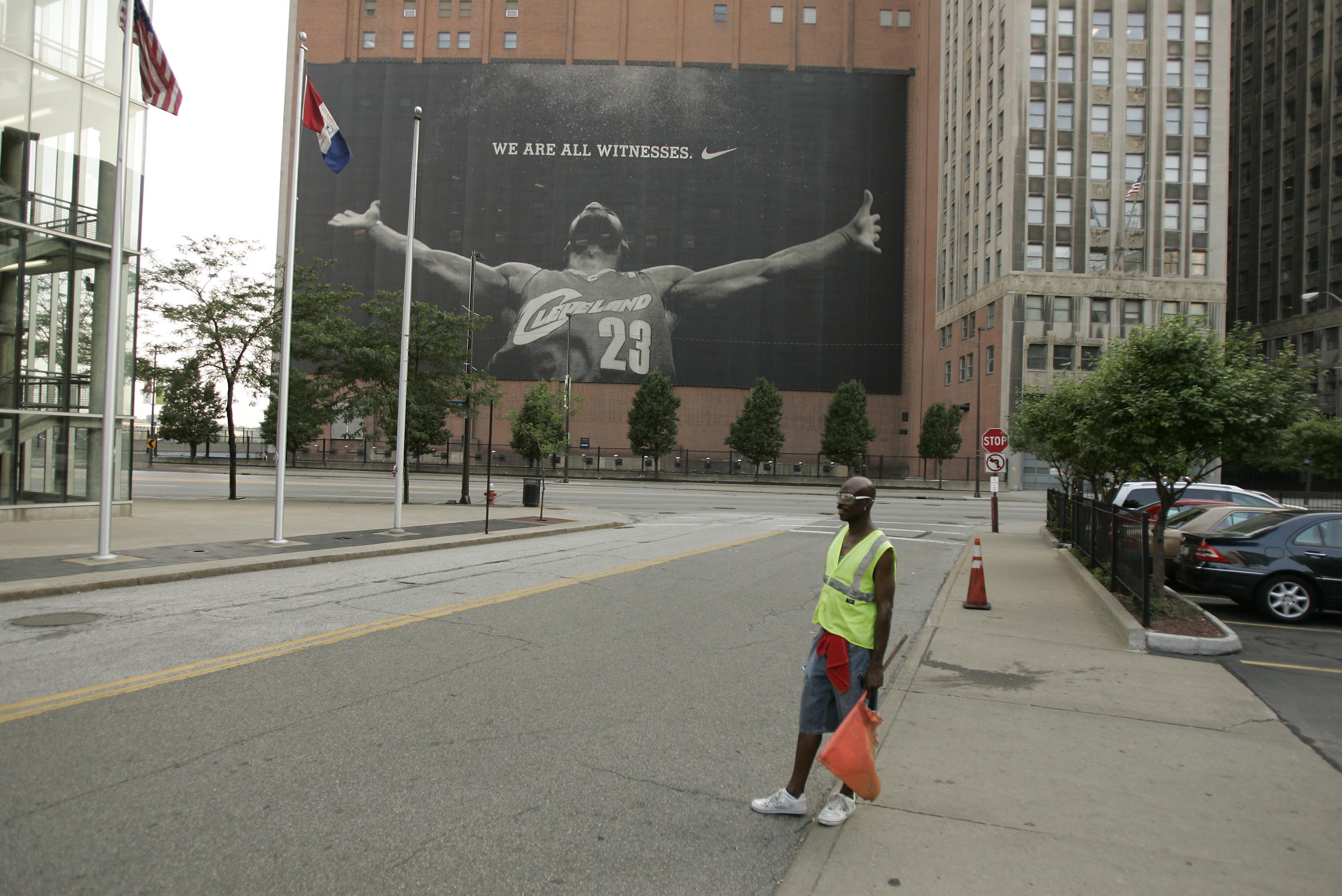 CLEVELAND - JULY 8:  A parking attendant stands near a larger than life photograph of LeBron James July 8, 2010 in Cleveland, Ohio. The two-time Most Valuable Player has the choice of remaining with the Cleveland Cavaliers or signing with a new team. (Pho