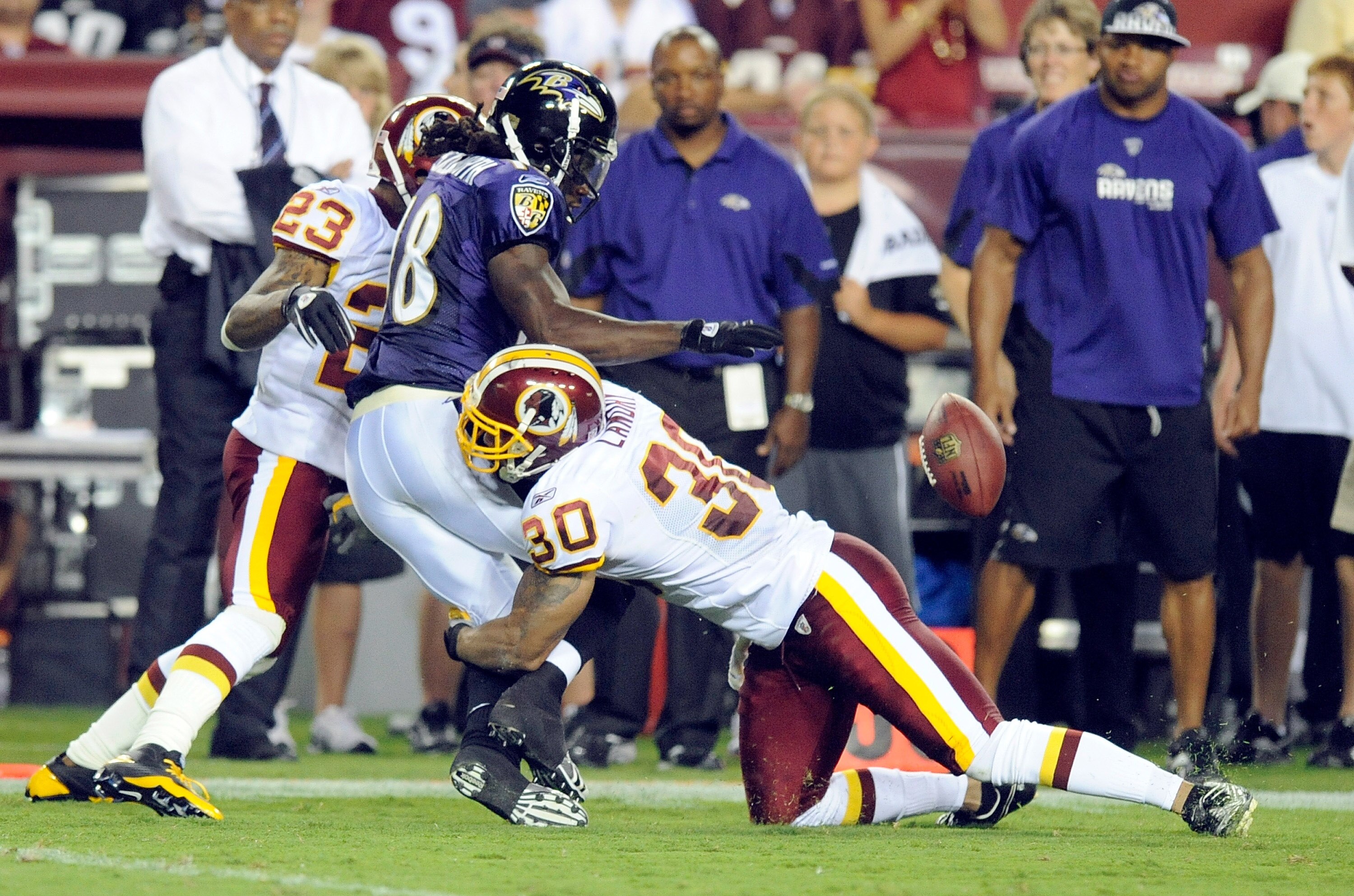 LANDOVER, MD - AUGUST 21:  Donte' Stallworth #18 of the Baltimore Ravens fumbles the ball during the preseason game after being hit by DeAngelo Hall #23 and LaRon Landry #30 of the Washington Redskins at FedExField on August 21, 2010 in Landover, Maryland
