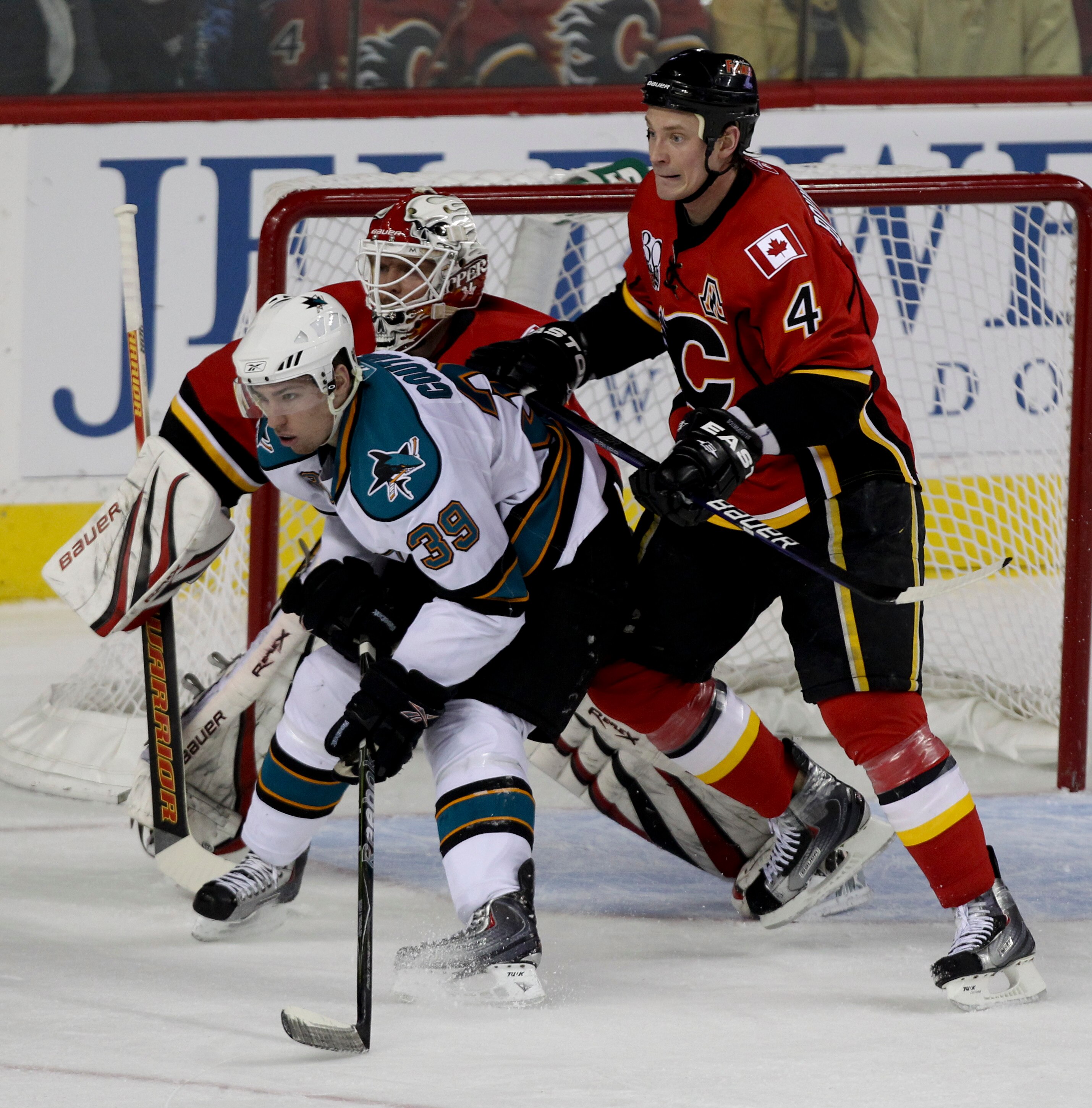 CALGARY, CANADA - APRIL 6:  Jay Bouwmeester #4 of the Calgary Flames tries to keep Logan Couture #39 of the San Jose Sharks away from goaltender Miikka Kiprusoff #34 in the first period of NHL action on April 6, 2010 at the Pengrowth Saddledome in Calgary