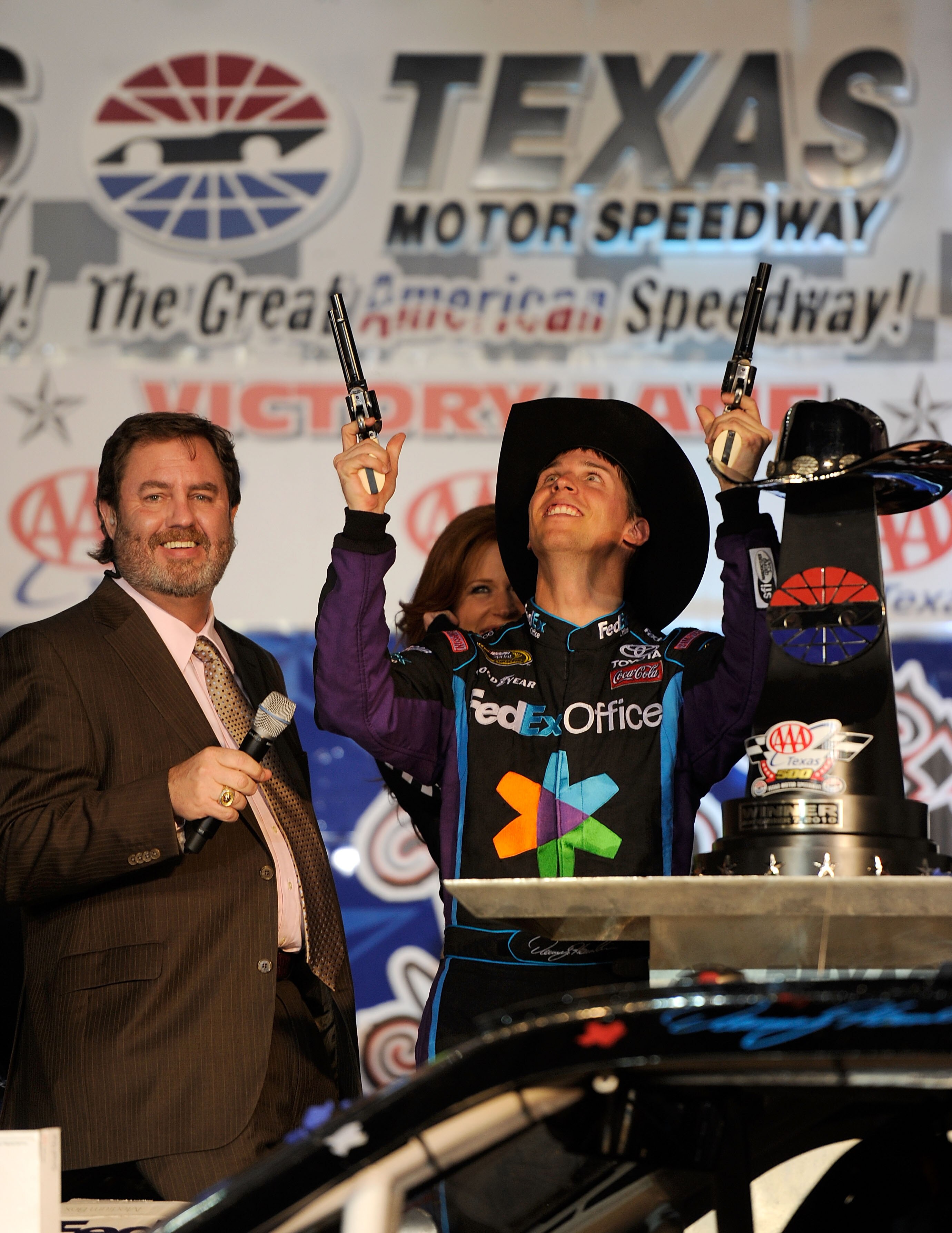 FORT WORTH, TX - NOVEMBER 07:  Texas Motor Speedway President Eddie Gossage (L) watches Denny Hamlin (C), driver of the #11 FedEx Office Toyota, as he shoots a Turnbull Revolvers in Victory Lane after winning the NASCAR Sprint Cup Series AAA Texas 500 at