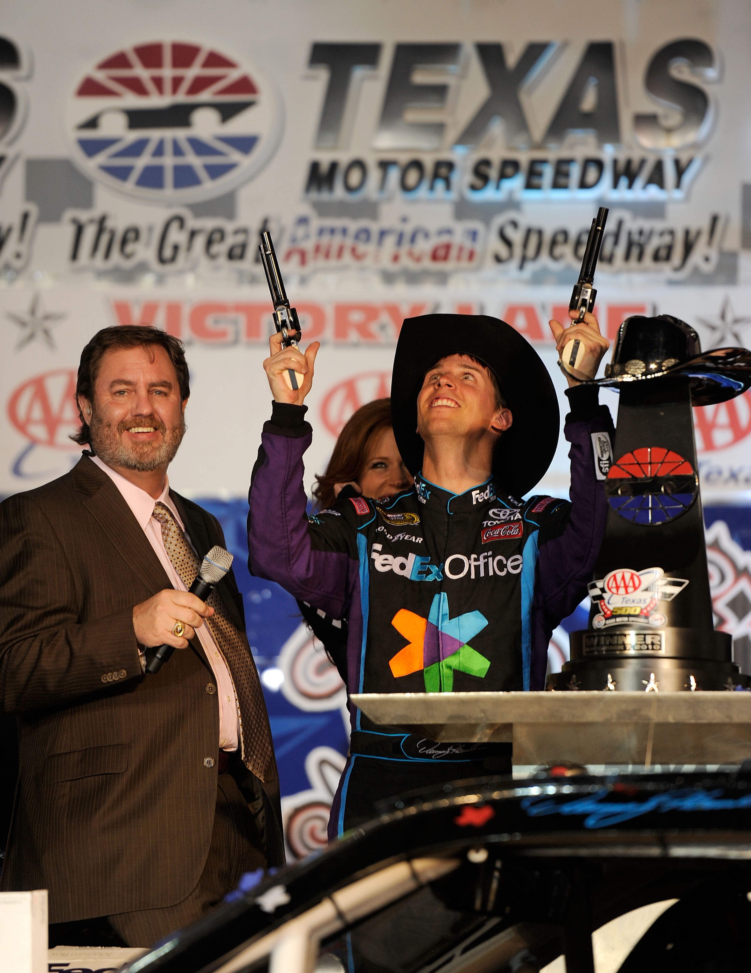 FORT WORTH, TX - NOVEMBER 07:  Texas Motor Speedway President Eddie Gossage (L) watches Denny Hamlin (C), driver of the #11 FedEx Office Toyota, as he shoots a Turnbull Revolvers in Victory Lane after winning the NASCAR Sprint Cup Series AAA Texas 500 at