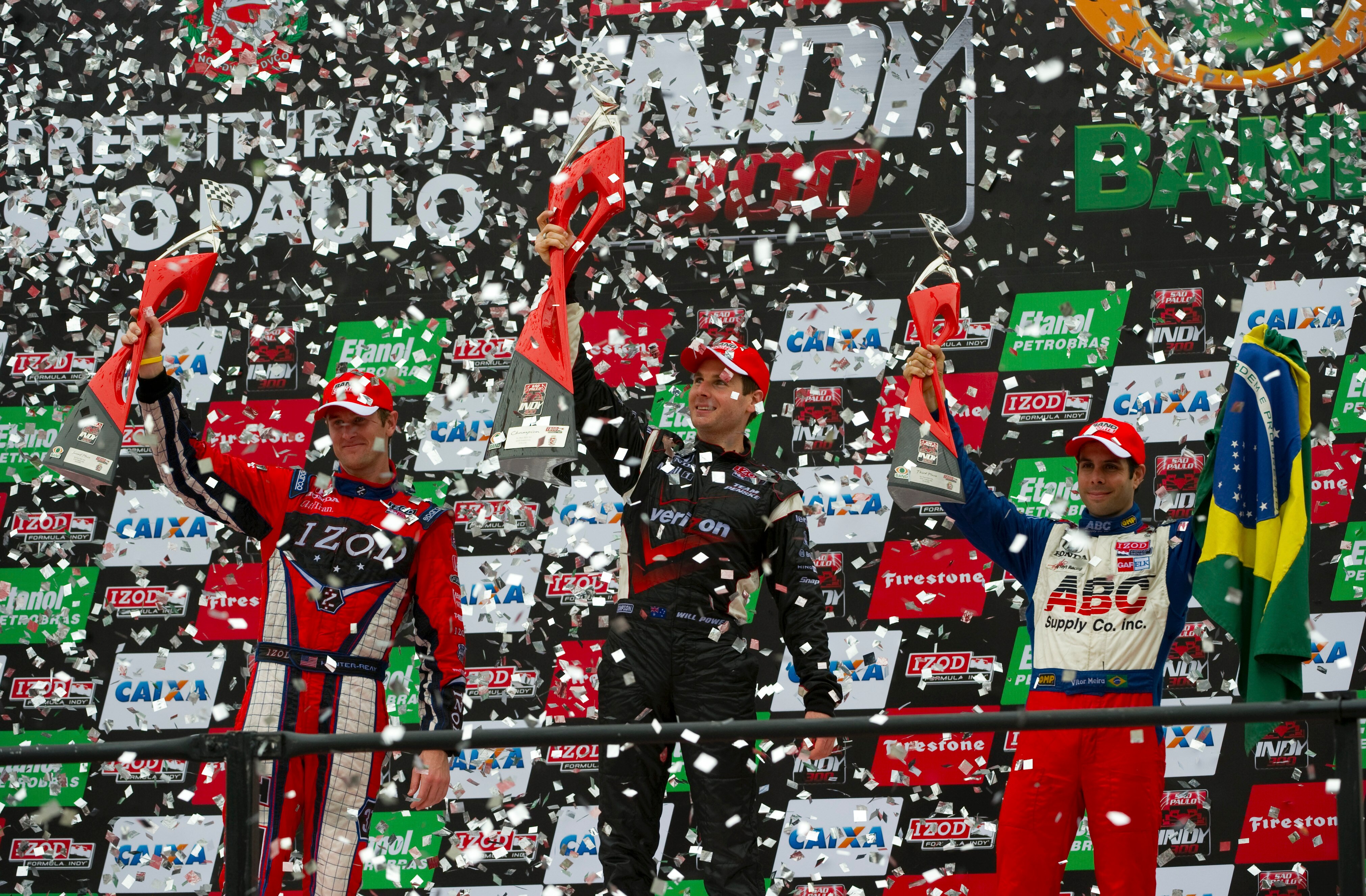 SAO PAULO, BRAZIL - MARCH 14:  Will Power (center) driver of the #12 Verizon Team Penske Dallara Honda lifts the winner's trophy on the podium after winning the IZOD IndyCar Series Sao Paulo Indy 300 as Ryan Hunter-Reay (left) in second place and Vitor Me