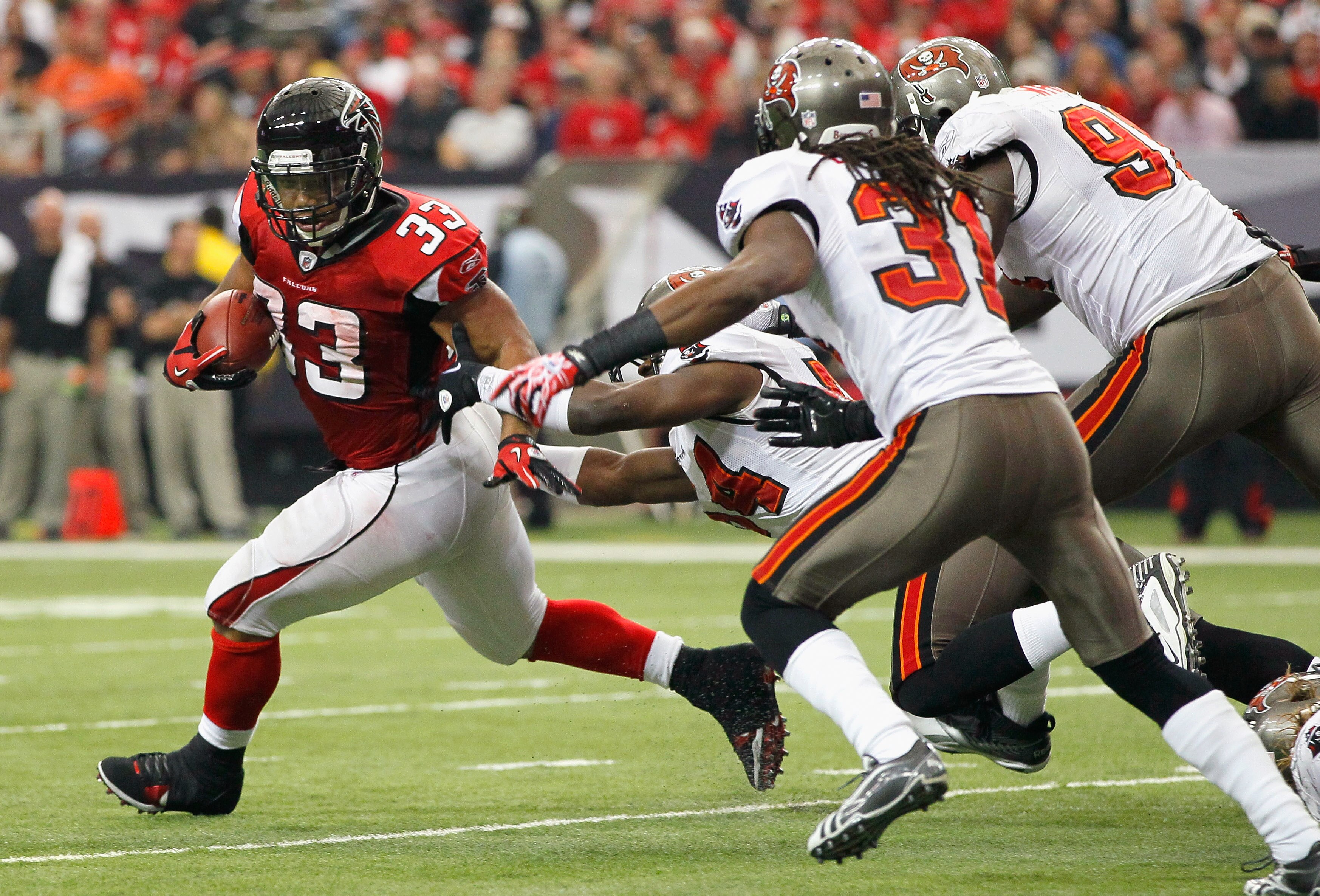 ATLANTA - NOVEMBER 07:  Michael Turner #33 of the Atlanta Falcons rushes away from Geno Hayes #54, E.J. Biggers #31 and Stylez G. White #91 of the Tampa Bay Buccaneers at Georgia Dome on November 7, 2010 in Atlanta, Georgia.  (Photo by Kevin C. Cox/Getty