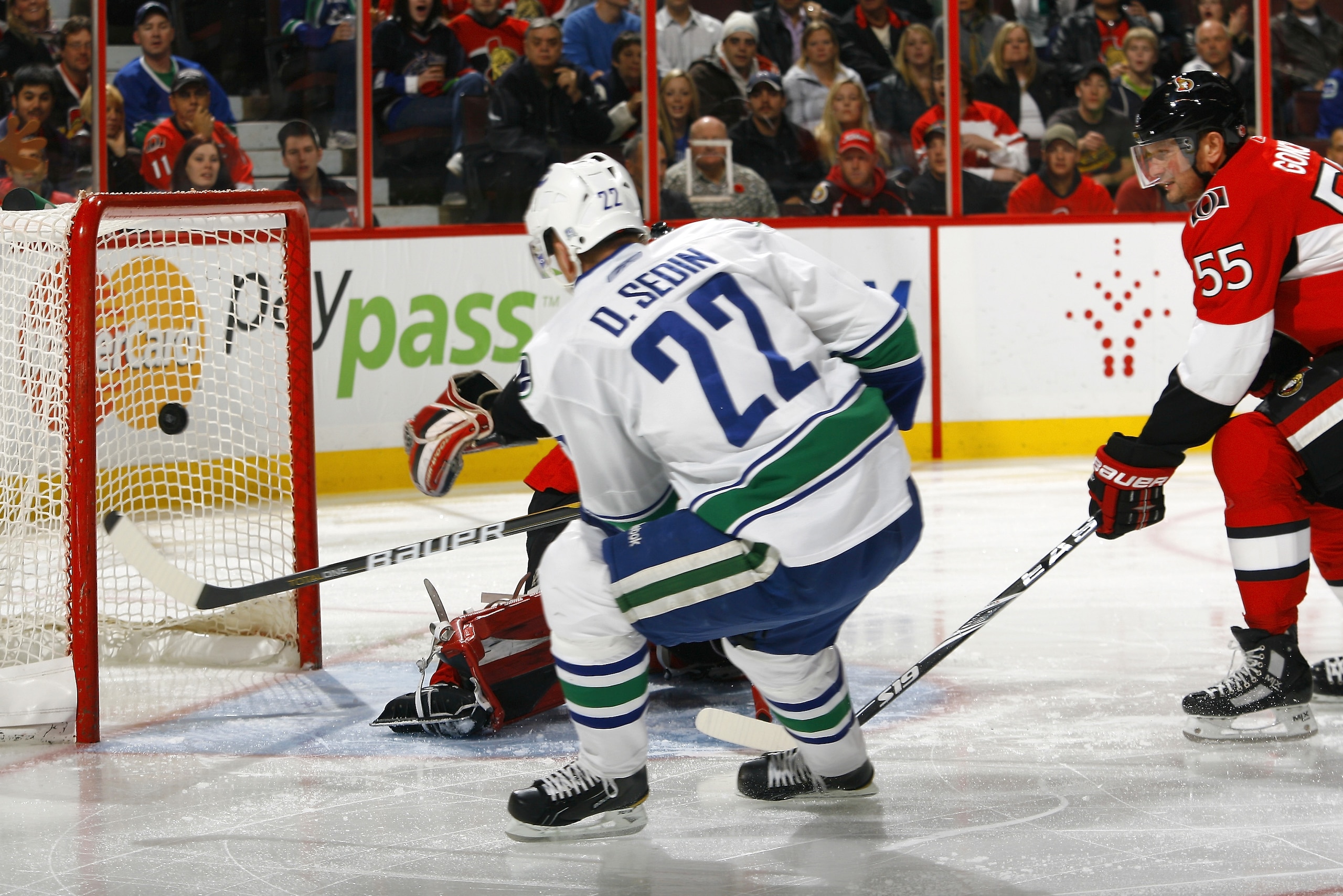 OTTAWA - NOVEMBER 11:  Daniel Sedin #22 of the Vancouver Canucks fires a shot into the net in behind Pascal Leclaire #33 of the Ottawa Senators while Sergei Gonchar #55 of the Senators looks on during a game at Scotiabank Place on November 11, 2010 in Ott