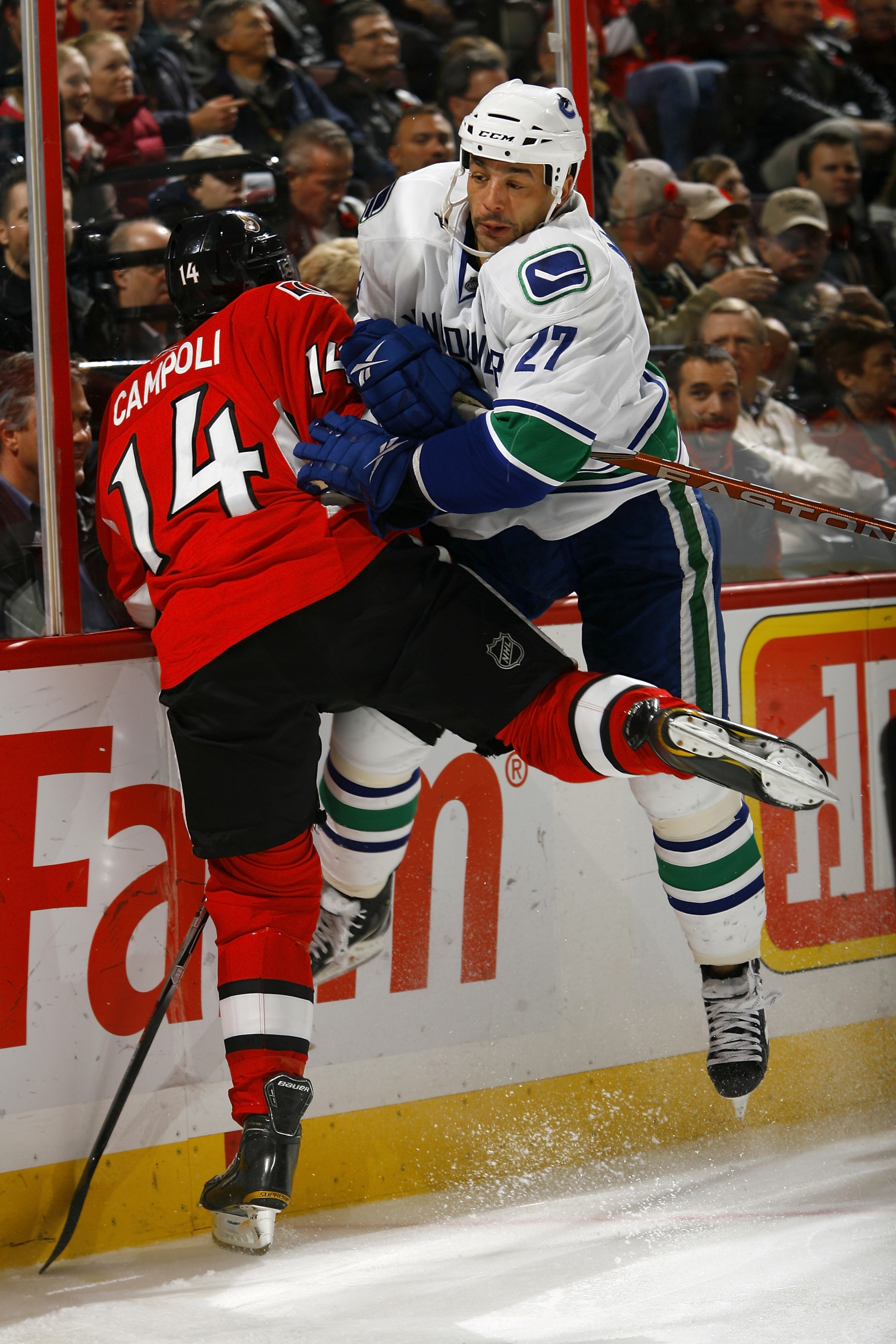 OTTAWA - NOVEMBER 11:  Manny Malhotra #27 of the Vancouver Canucks throws a bodycheck on Chris Campoli #14 of the Ottawa Senators along the end boards in a game at Scotiabank Place on November 11, 2010 in Ottawa, Ontario, Canada.  The Vancouver Canucks de