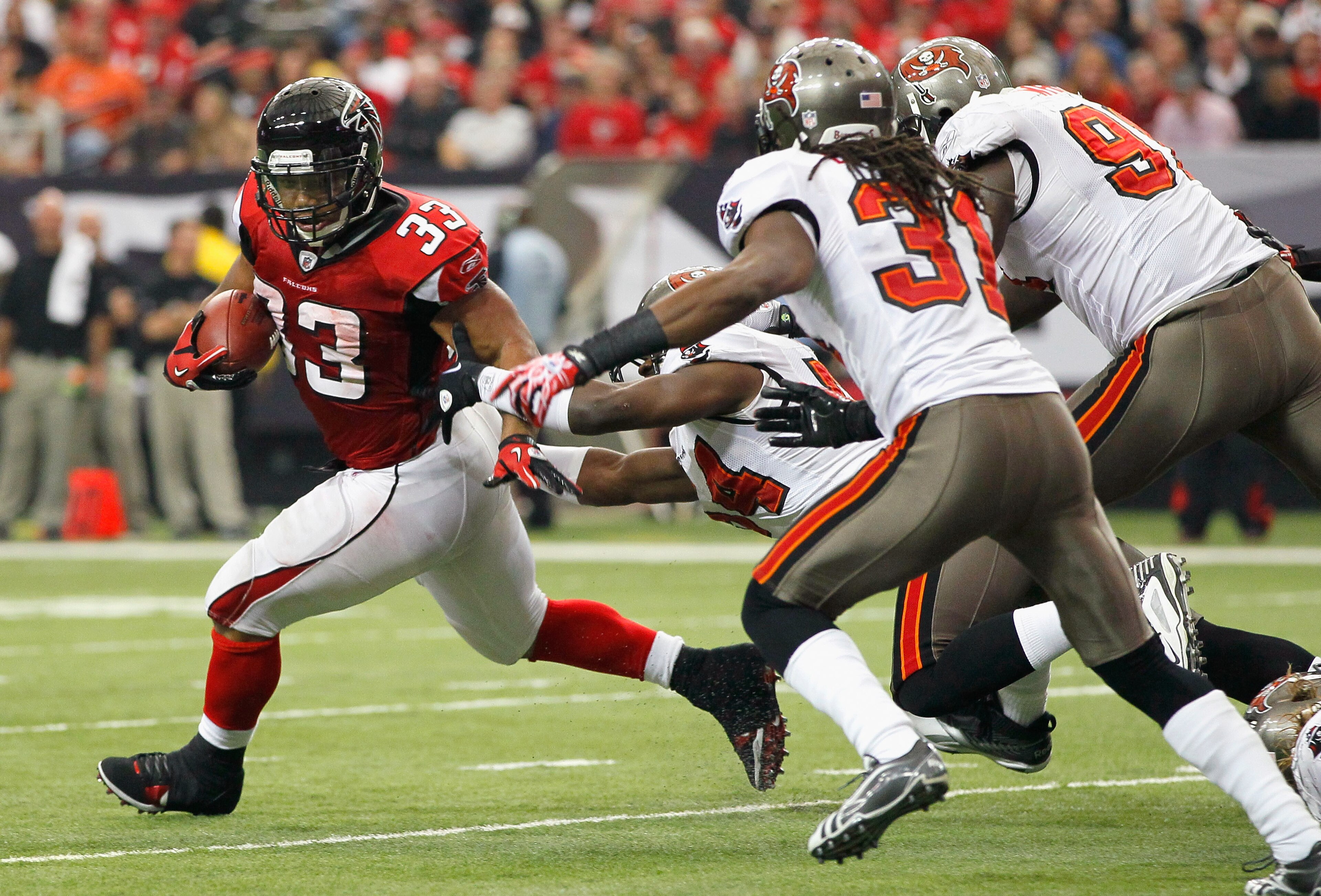 ATLANTA - NOVEMBER 07:  Michael Turner #33 of the Atlanta Falcons rushes away from Geno Hayes #54, E.J. Biggers #31 and Stylez G. White #91 of the Tampa Bay Buccaneers at Georgia Dome on November 7, 2010 in Atlanta, Georgia.  (Photo by Kevin C. Cox/Getty