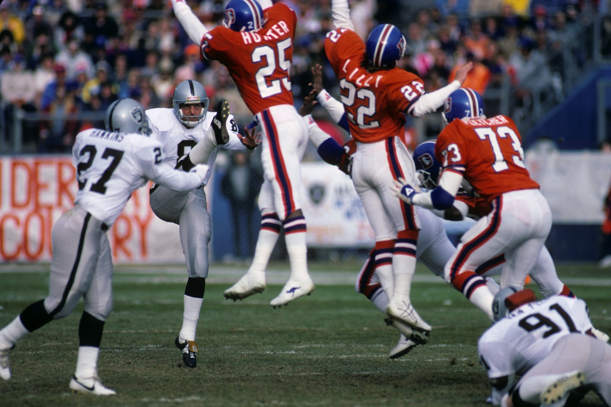 DENVER - DECEMBER 8:  Punter Ray Guy #8 of the Los Angeles Raiders kicks the ball away against defensive backs Daniel Hunter #25, Tony Lilly #22 and linebacker Simon Fletcher #73 of the Denver Broncos during the game at Mile High Stadium on December 8, 19