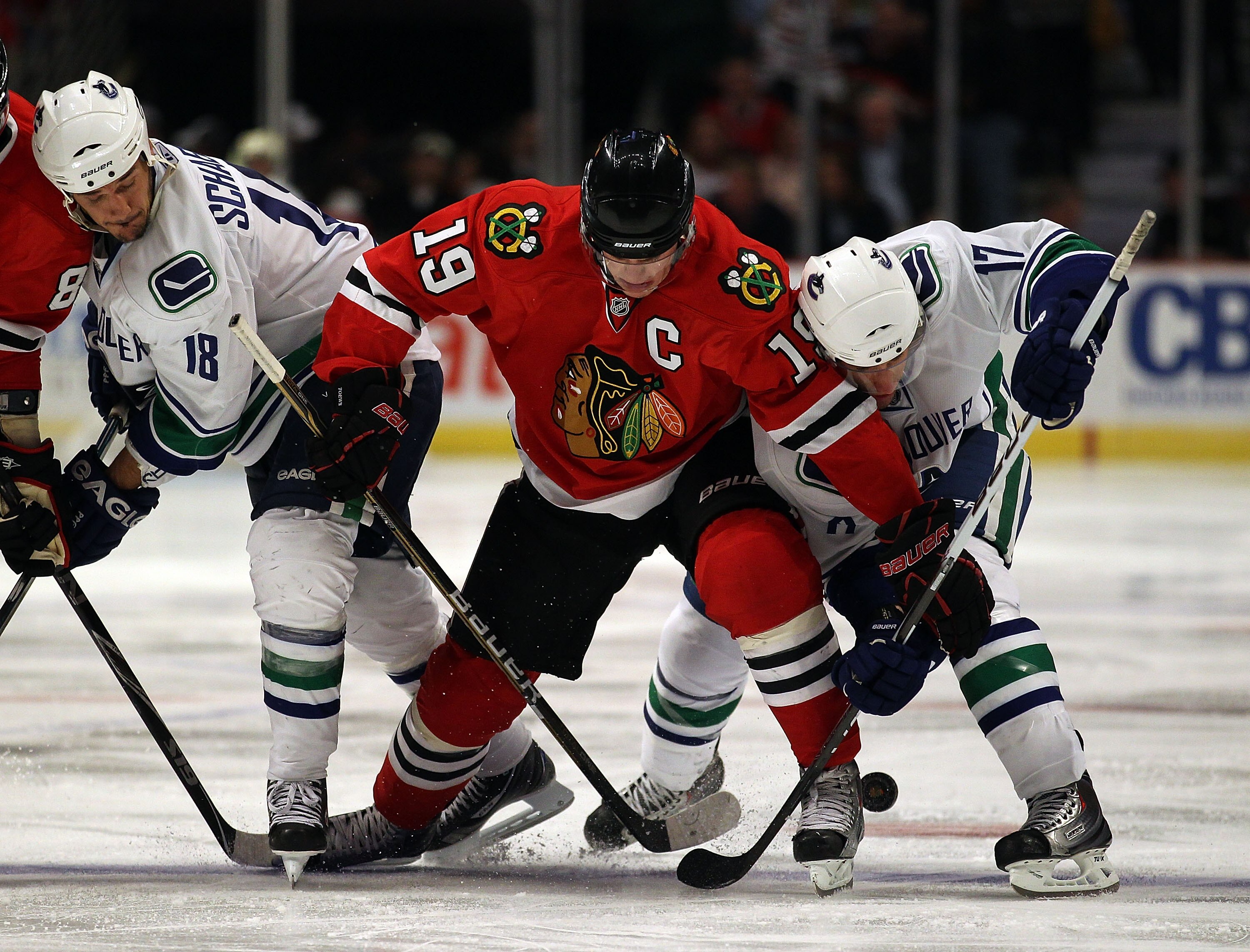 CHICAGO - OCTOBER 20: Jonathan Toews #19 of the Chicago Blackhawks battles for the puck with Peter Schaefer #18 (L) and Ryan Kesler #17 of the Vancouver Canucks at the United Center on October 20, 2010 in Chicago, Illinois. The Blackhawks defeated the Can