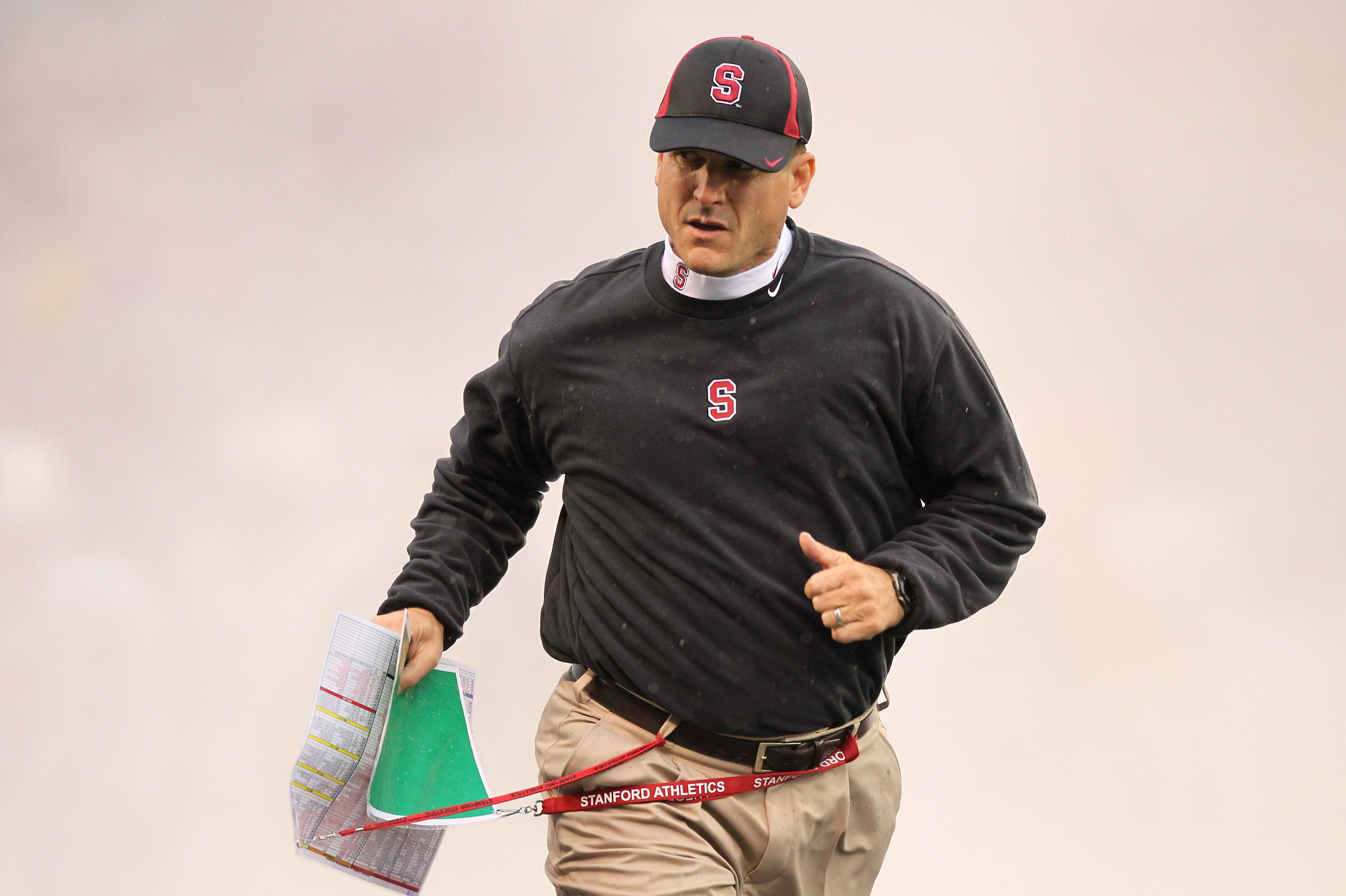 SEATTLE - OCTOBER 30:  Head coach Jim Harbaugh of the Stanford Cardinal runs through a smoke screen as he takes the field prior to the game against the Washington Huskies on October 30, 2010 at Husky Stadium in Seattle, Washington. Stanford won 41-0. (Pho