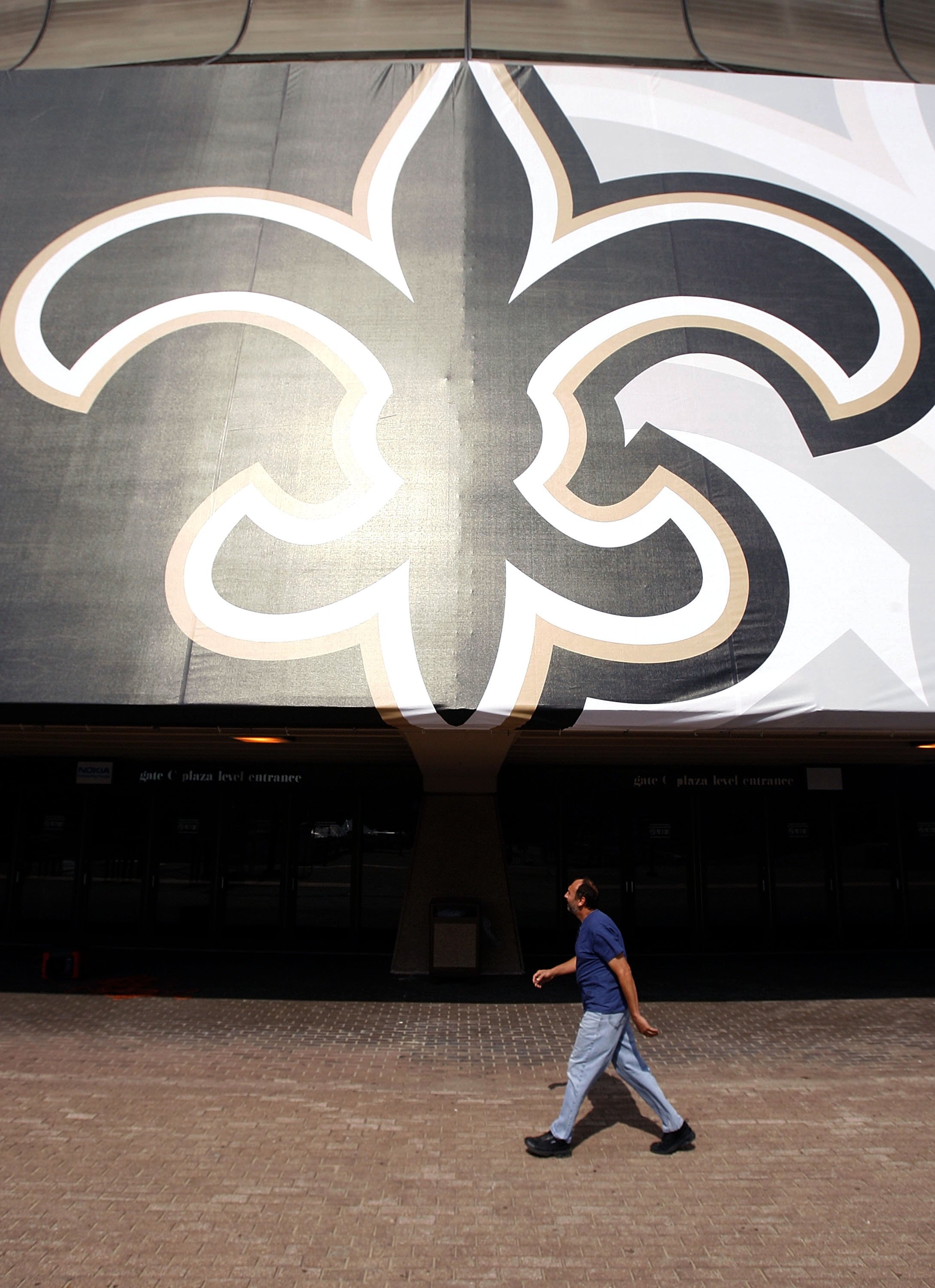 NEW ORLEANS - SEPTEMBER 23:  A pedestrian walks past a giant Fleur-de-Lis outside the Louisiana Superdome as it prepares to reopen on September 23, 2006 in New Orleans, Louisiana.  The Superdome will reopen for the first NFL New Orleans Saints game agains