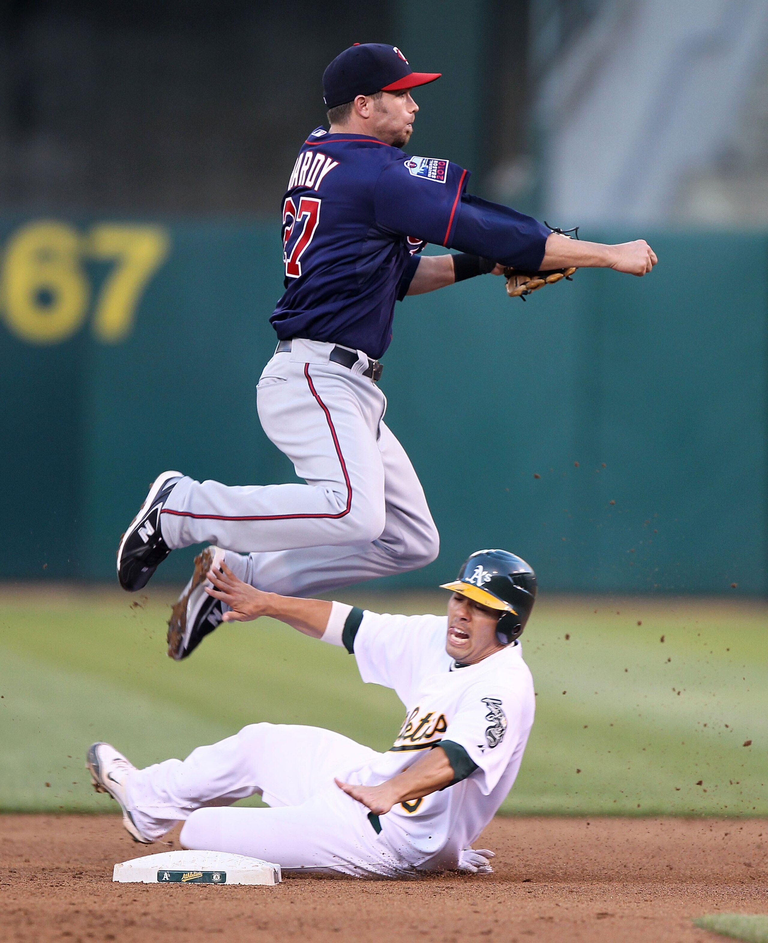 OAKLAND, CA - JUNE 04:  J.J. Hardy #27 of the Minnesota Twins leaps over Kurt Suzuki #8 of the Oakland Athletics on a double play hit by Jack Cust in the fourth inning during an MLB game at the Oakland-Alameda County Coliseum on June 4, 2010 in Oakland, C