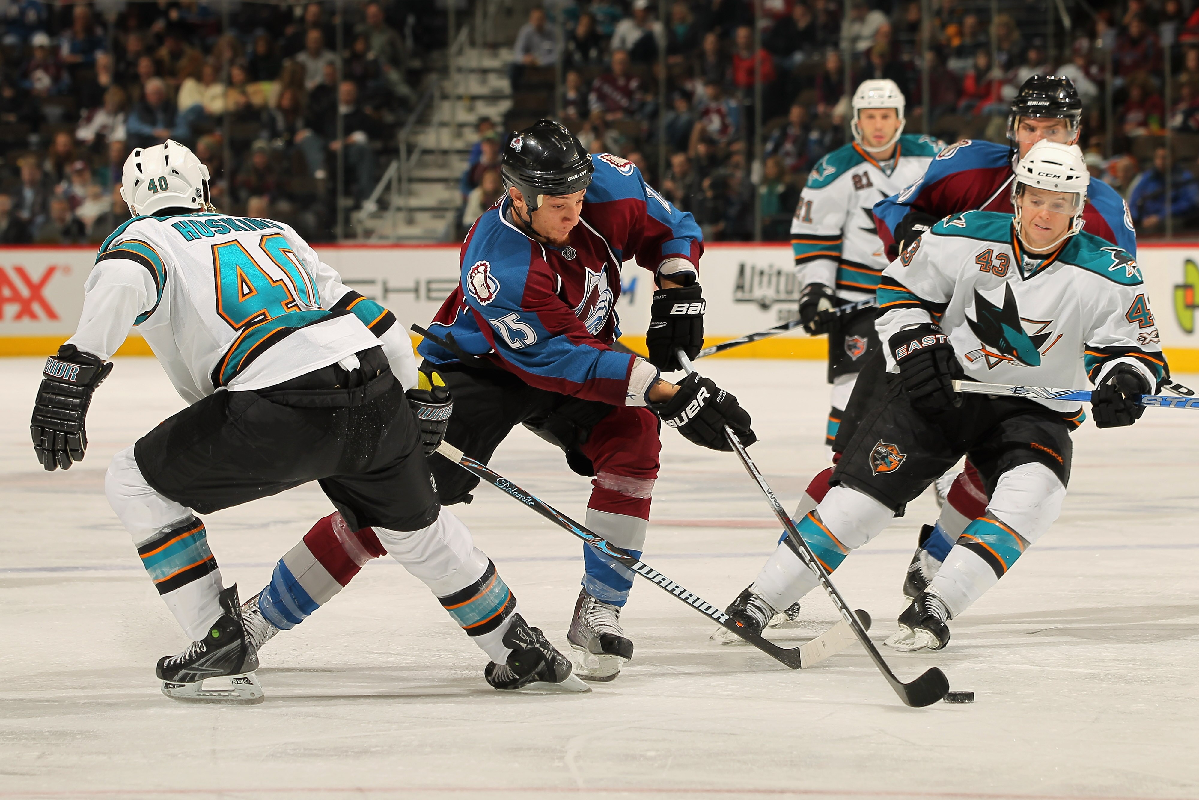 DENVER - NOVEMBER 17:  Chris Stewart #25 of the Colorado Avalanche controls the puck between Kent Huskins #40 and John McCarthy #43 of the San Jose Sharks at the Pepsi Center on November 17, 2010 in Denver, Colorado. The Avalanche defeated the Sharks 4-3