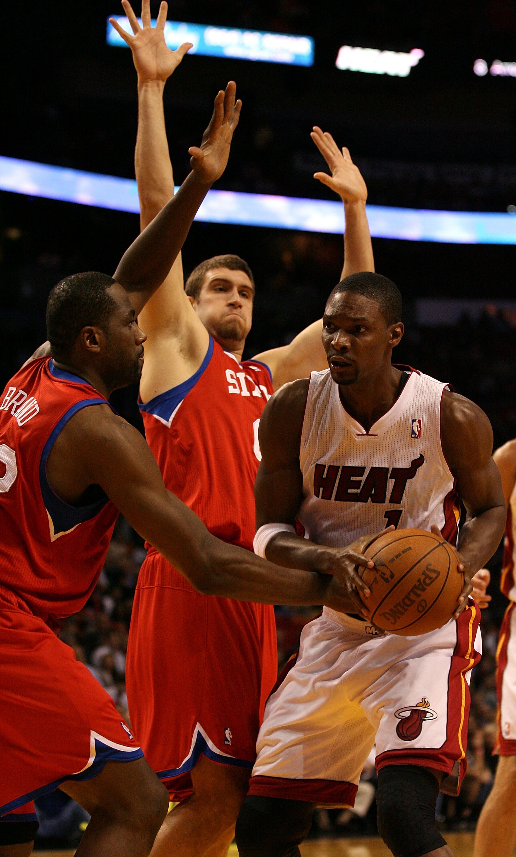 MIAMI - NOVEMBER 26:  Forward Chris Bosh #1 of the Miami Heat drives against center Spencer Hawes #00 and forward Elton Brand #42 of the Philadelphia 76ers at American Airlines Arena on November 26, 2010 in Miami, Florida. The Heat defeated the 76ers 99-9