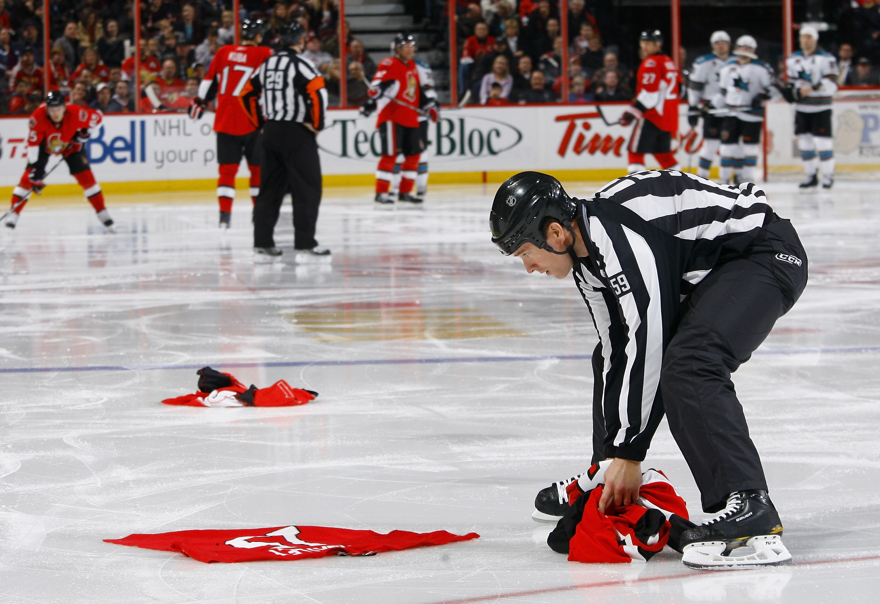 OTTAWA, ON - DECEMBER 02:  Linesman Steve Barton (59) picks up a selection of discarded Dany Heatley Ottawa Senators jerseys that were thrown onto the ice in discontent in a game between the San Jose Sharks and the Ottawa Senators at Scotiabank Place on D