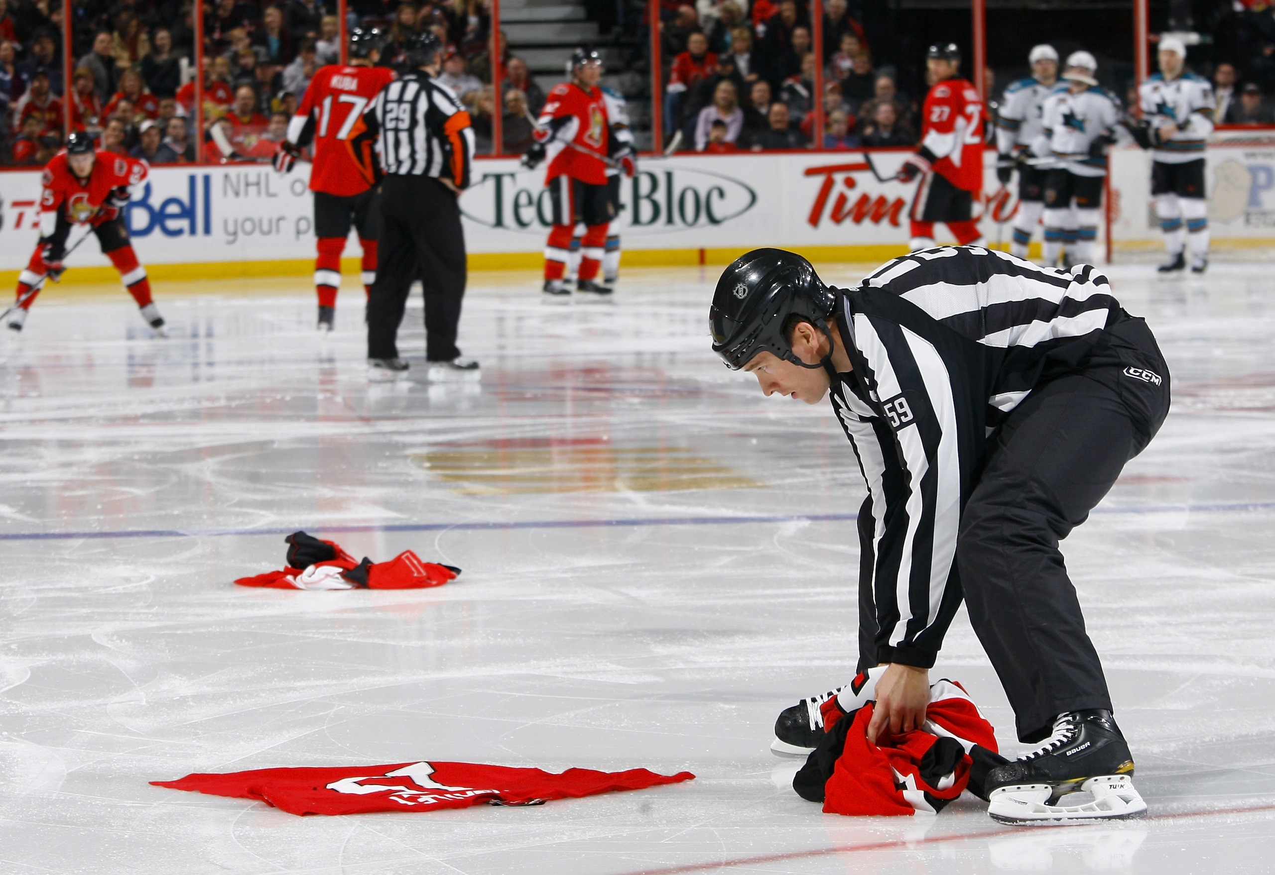 OTTAWA, ON - DECEMBER 02:  Linesman Steve Barton (59) picks up a selection of discarded Dany Heatley Ottawa Senators jerseys that were thrown onto the ice in discontent in a game between the San Jose Sharks and the Ottawa Senators at Scotiabank Place on D