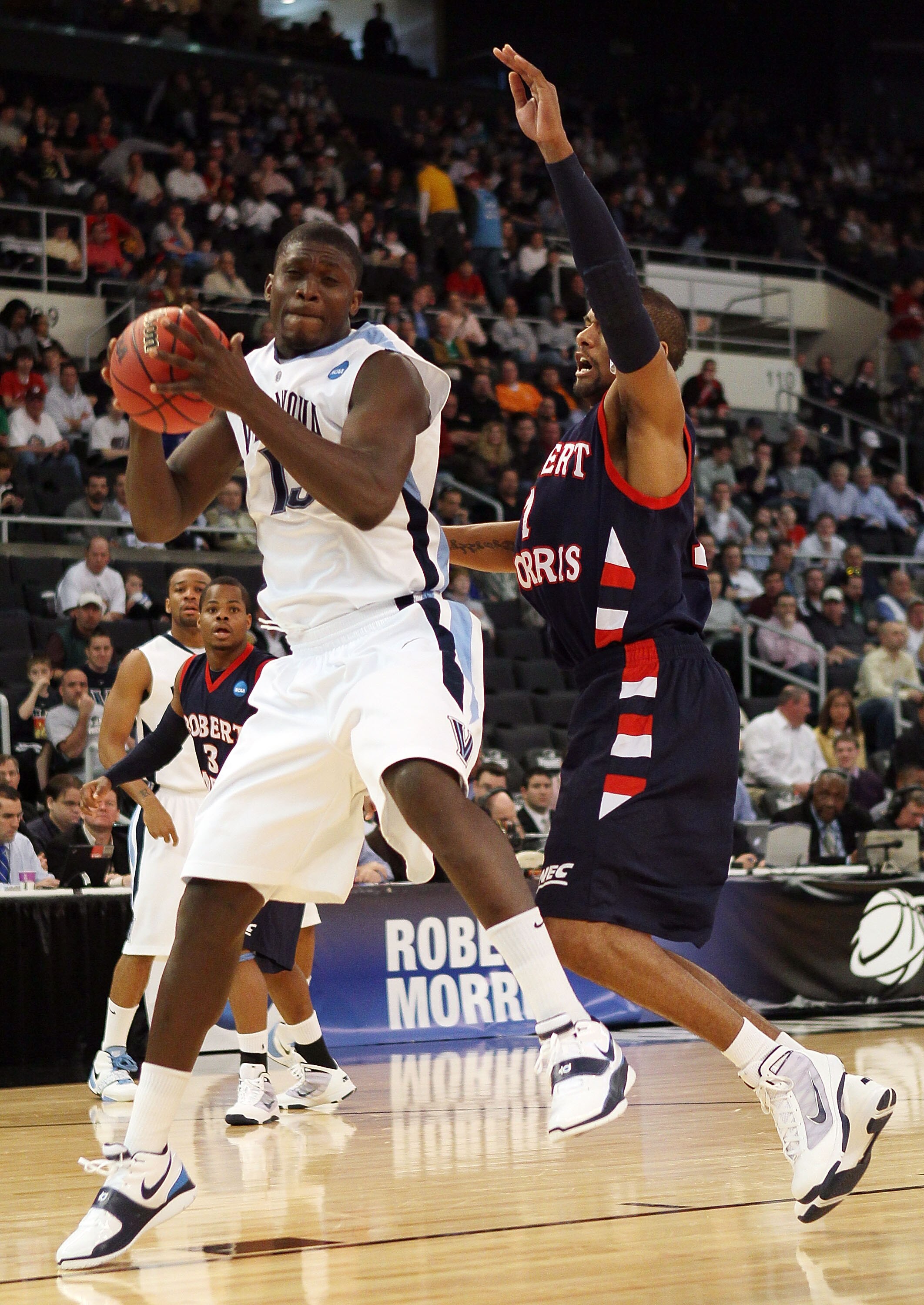PROVIDENCE, RI - MARCH 18:  Mouphtaou Yarou #13  of the Villanova Wildcats heads for the basket as Rob Robinson #1 of the Robert Morris Colonials defends during the first round of the 2010 NCAA men's basketball tournament on March 18, 2010 at the Dunkin D