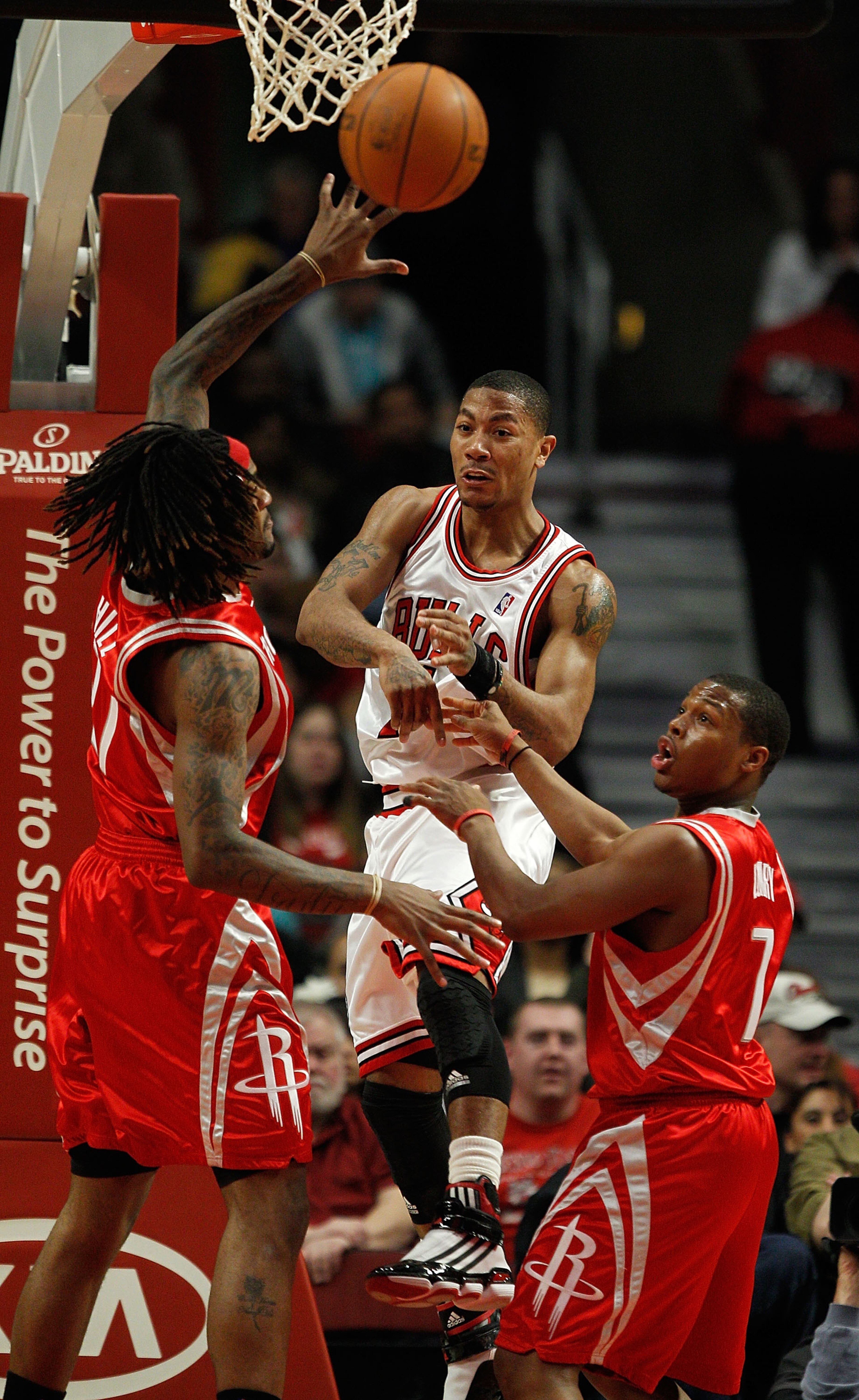 CHICAGO - MARCH 22: Derrick Rose #1 of the Chicago Bulls leaps to pass the ball between Jordan Hill #27 and Kyle Lowry #7 of the Houston Rockets at the United Center on March 22, 2010 in Chicago, Illinois. NOTE TO USER: User expressly acknowledges and agr