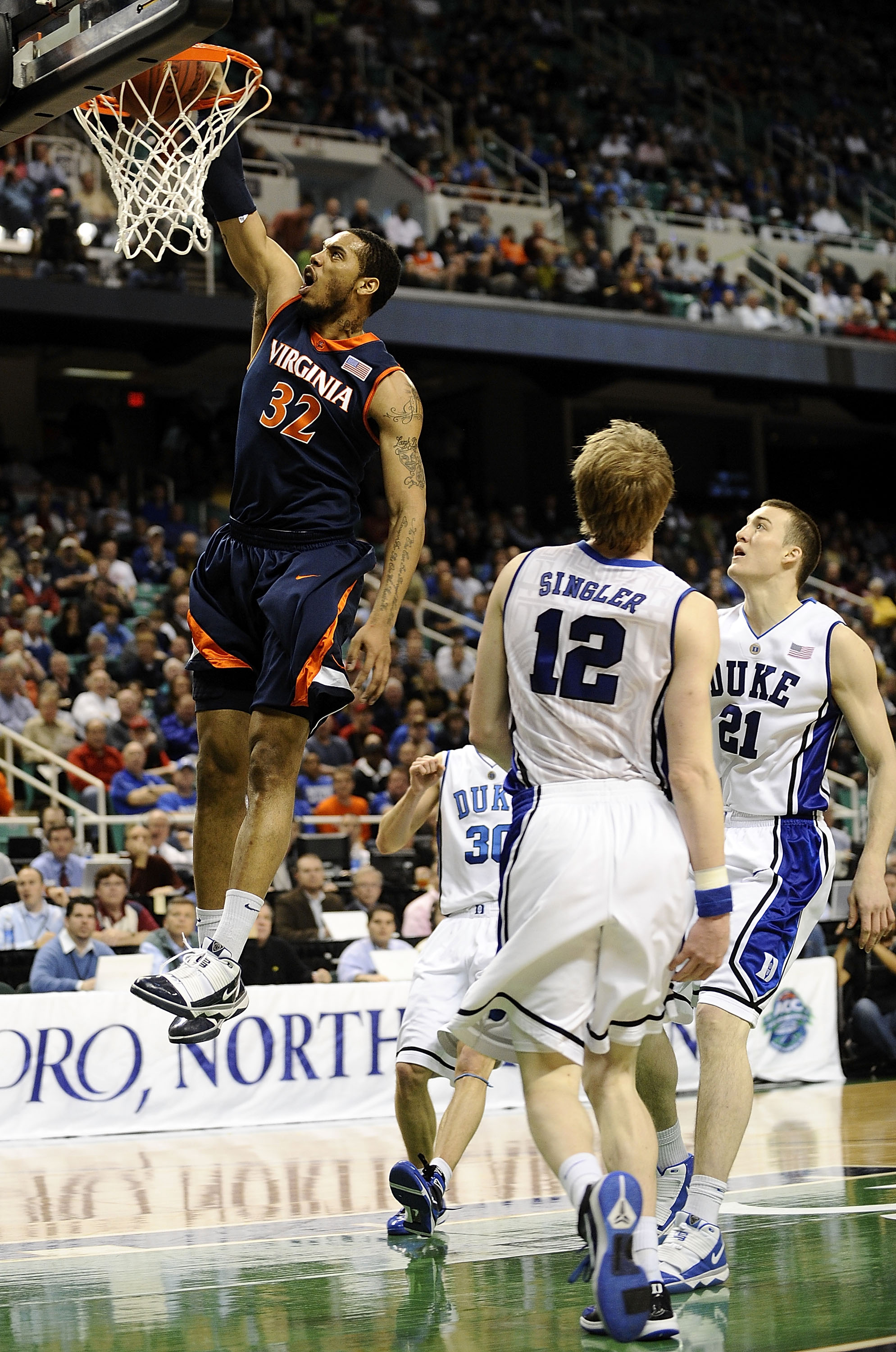 GREENSBORO, NC - MARCH 12:  Mike Scott #32 of the University of Virginia Cavaliers drives by Miles Plumlee #21 and Kyle Singler #12  of the Duke Blue Devils guards in their quarterfinal game in the 2010 ACC Men's Basketball Tournament at the Greensboro Co