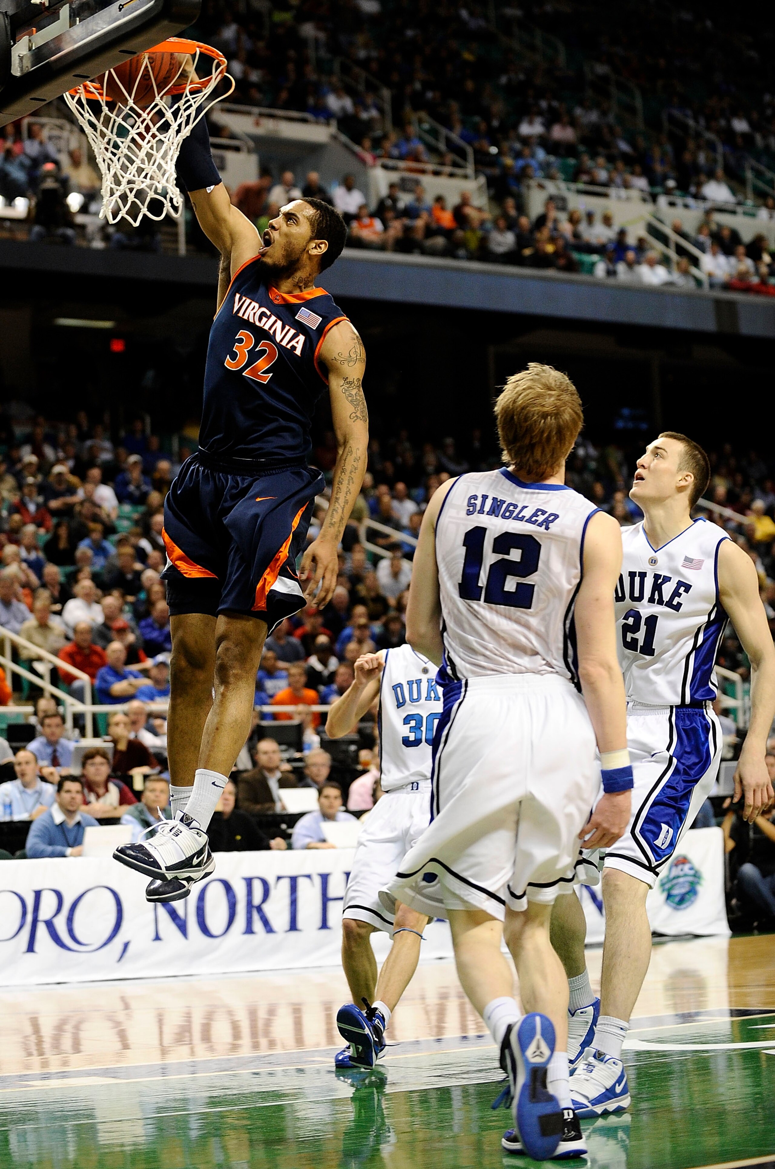 GREENSBORO, NC - MARCH 12: Mike Scott #32 of the University of Virginia Cavaliers drives by Miles Plumlee #21 and Kyle Singler #12 of the Duke Blue Devils guards in their quarterfinal game in the 2010 ACC Men's Basketball Tournament at the Greensboro Co GREENSBORO, NC - MARCH 12: Mike Scott #32 of the University of Virginia Cavaliers drives by Miles Plumlee #21 and Kyle Singler #12 of the Duke Blue Devils guards in their quarterfinal game in the 2010 ACC Men's Basketball Tournament at the Greensboro Co