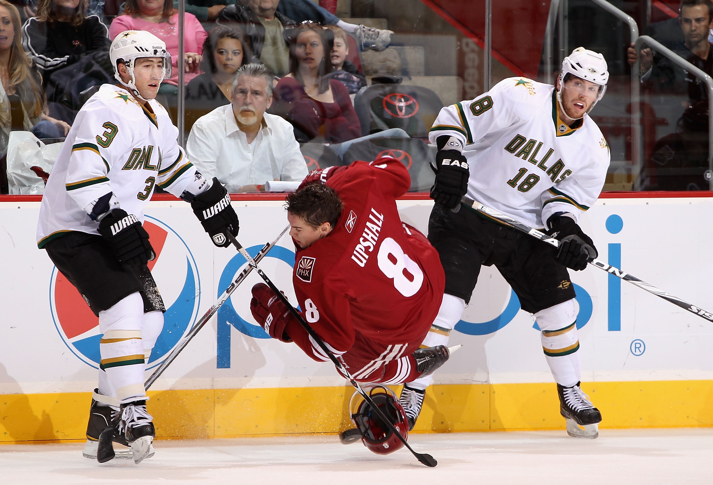 GLENDALE, AZ - DECEMBER 11:  Scottie Upshall #8 of the Phoenix Coyotes is tripped up as he battles for the puck with Stephane Robidas #3 and James Neal #18 of the Dallas Stars during the NHL game at Jobing.com Arena on December 11, 2010 in Glendale, Arizo