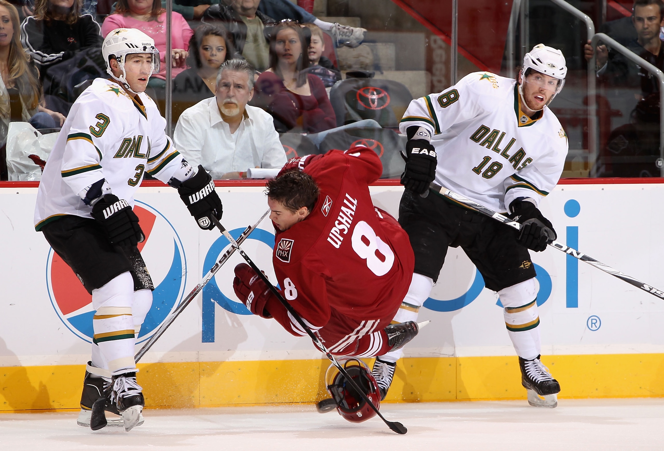 GLENDALE, AZ - DECEMBER 11:  Scottie Upshall #8 of the Phoenix Coyotes is tripped up as he battles for the puck with Stephane Robidas #3 and James Neal #18 of the Dallas Stars during the NHL game at Jobing.com Arena on December 11, 2010 in Glendale, Arizo