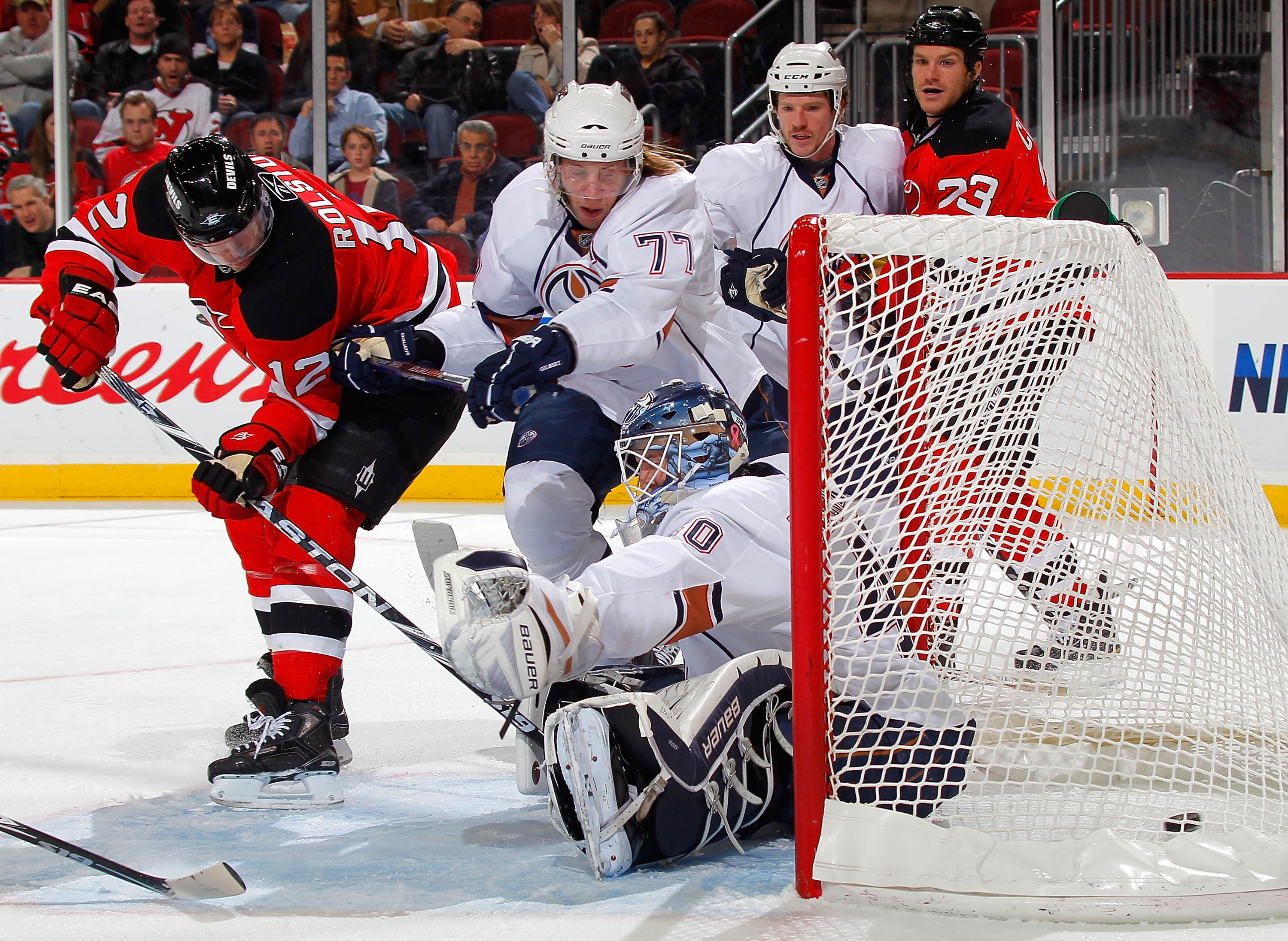 NEWARK, NJ - NOVEMBER 12:  Tom Gilbert #77 of the Edmonton Oilers tries to defend against Brian Rolston #12 of the New Jersey Devils as he shoots the puck past goalie Devan Dubnyk #40 of the Oilers during the second period of a hockey game at the Prudenti