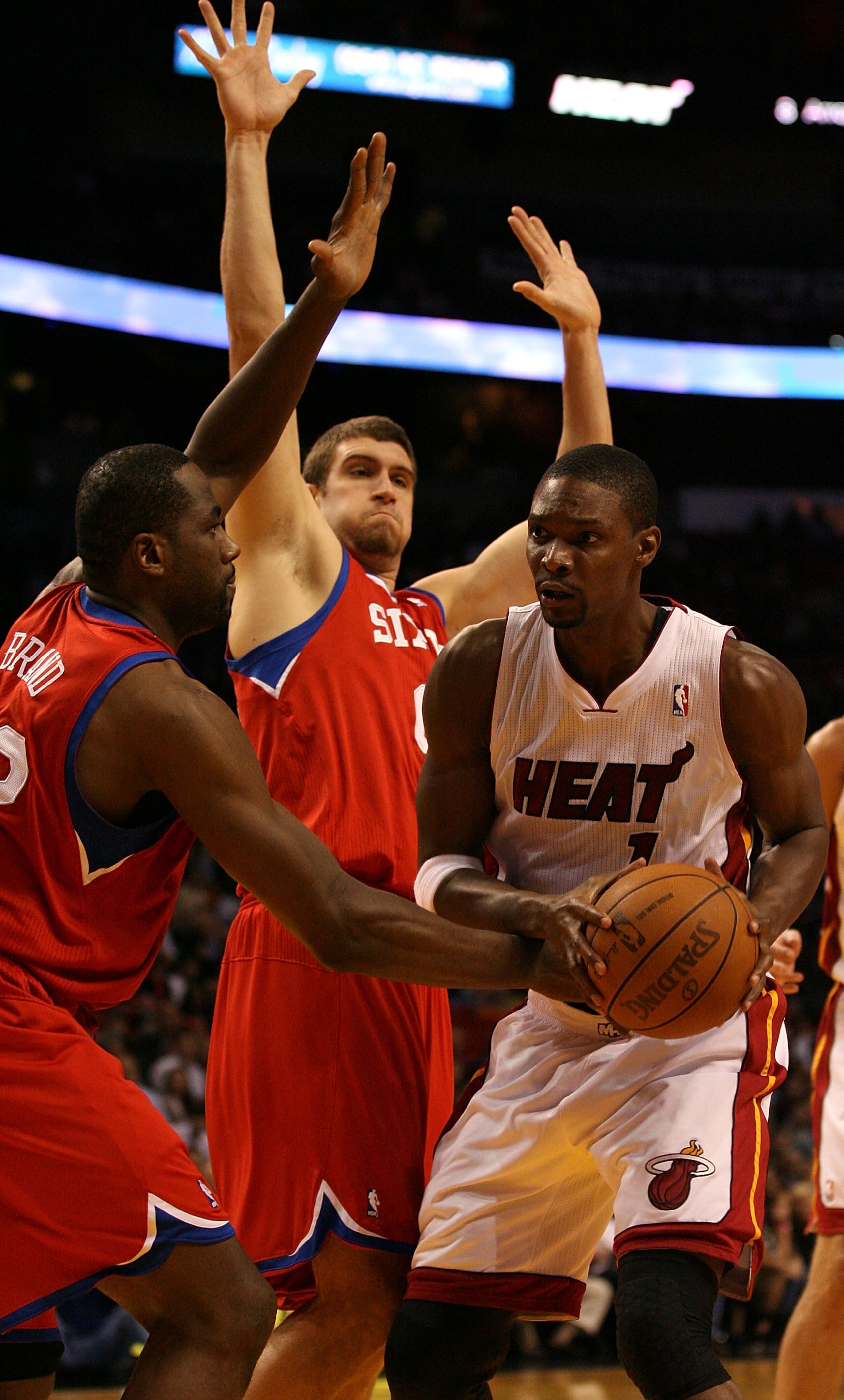 MIAMI - NOVEMBER 26:  Forward Chris Bosh #1 of the Miami Heat drives against center Spencer Hawes #00 and forward Elton Brand #42 of the Philadelphia 76ers at American Airlines Arena on November 26, 2010 in Miami, Florida. The Heat defeated the 76ers 99-9